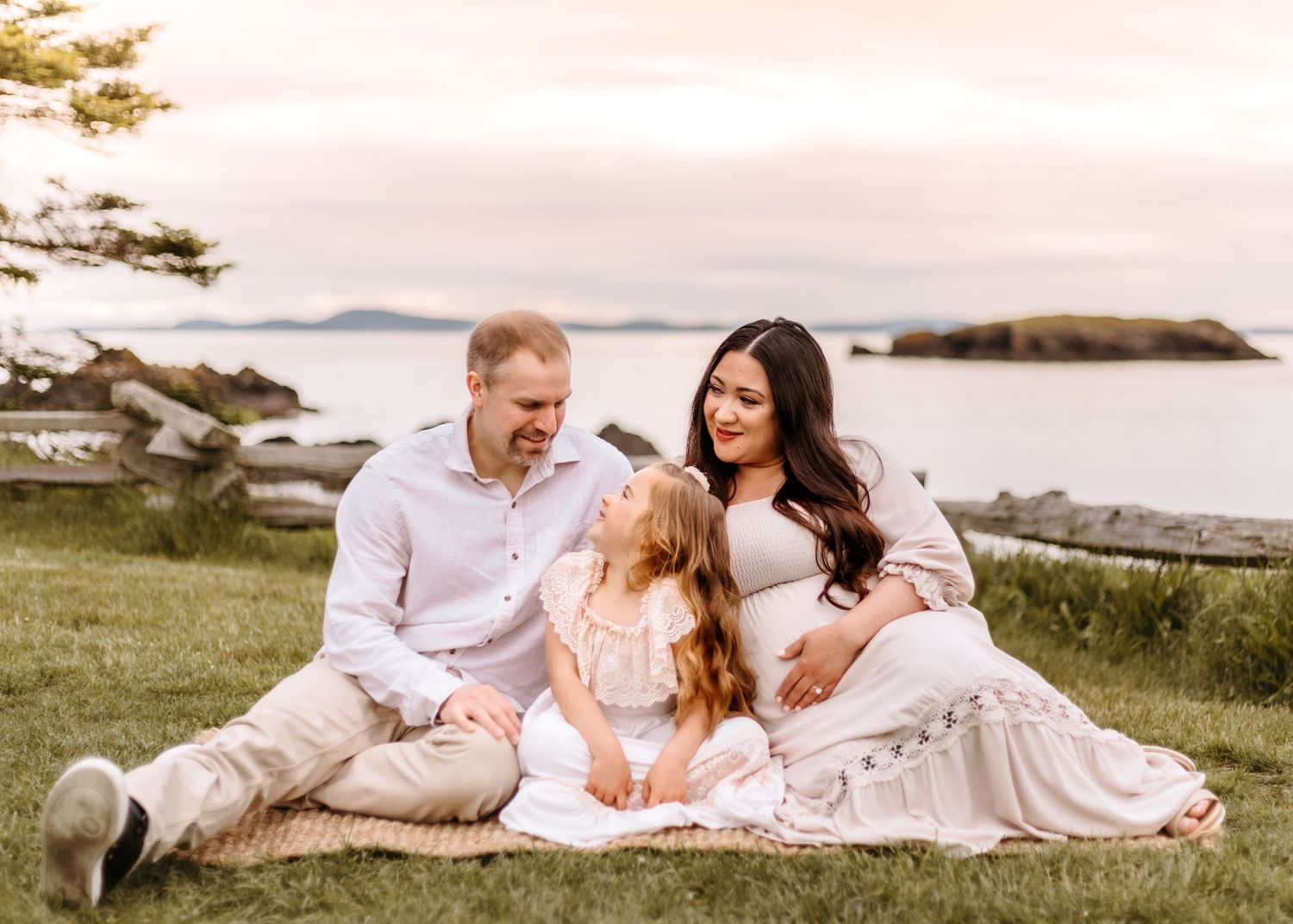 Family of three having picnic on grassy hill overlooking ocean islands.