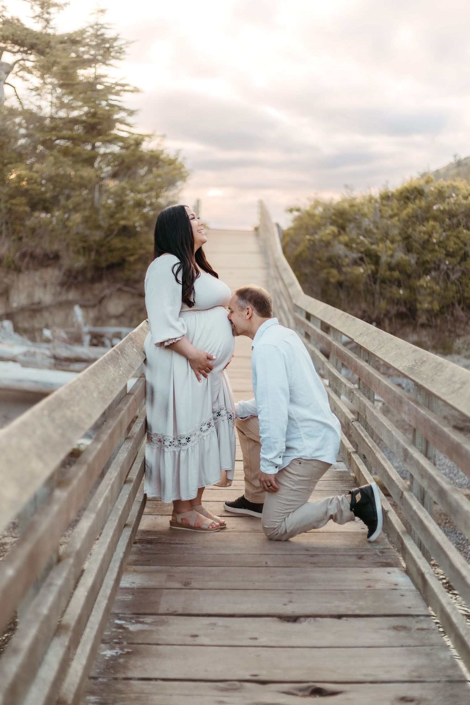 Sweet maternity moment captured on wooden boardwalk during sunset photoshoot.