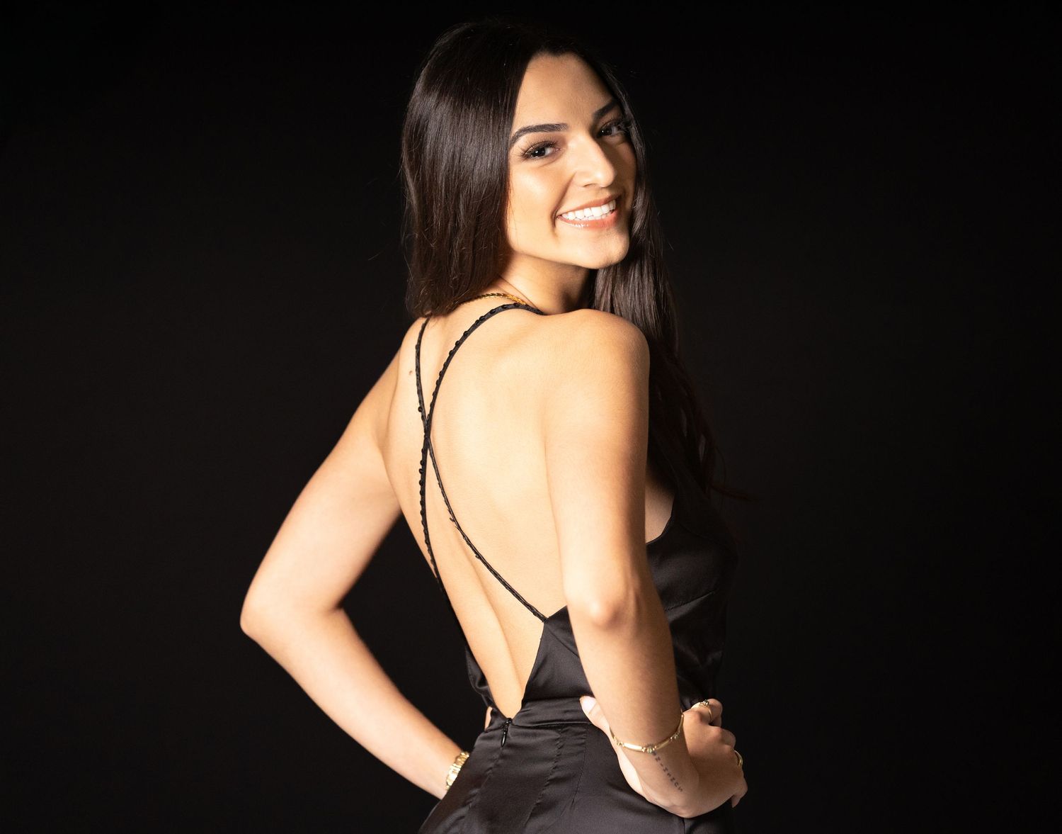 Elegant black backless evening dress photographed against dark background.
