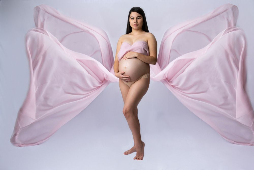 Pregnant woman with flowing pink fabric wings in studio maternity shoot.