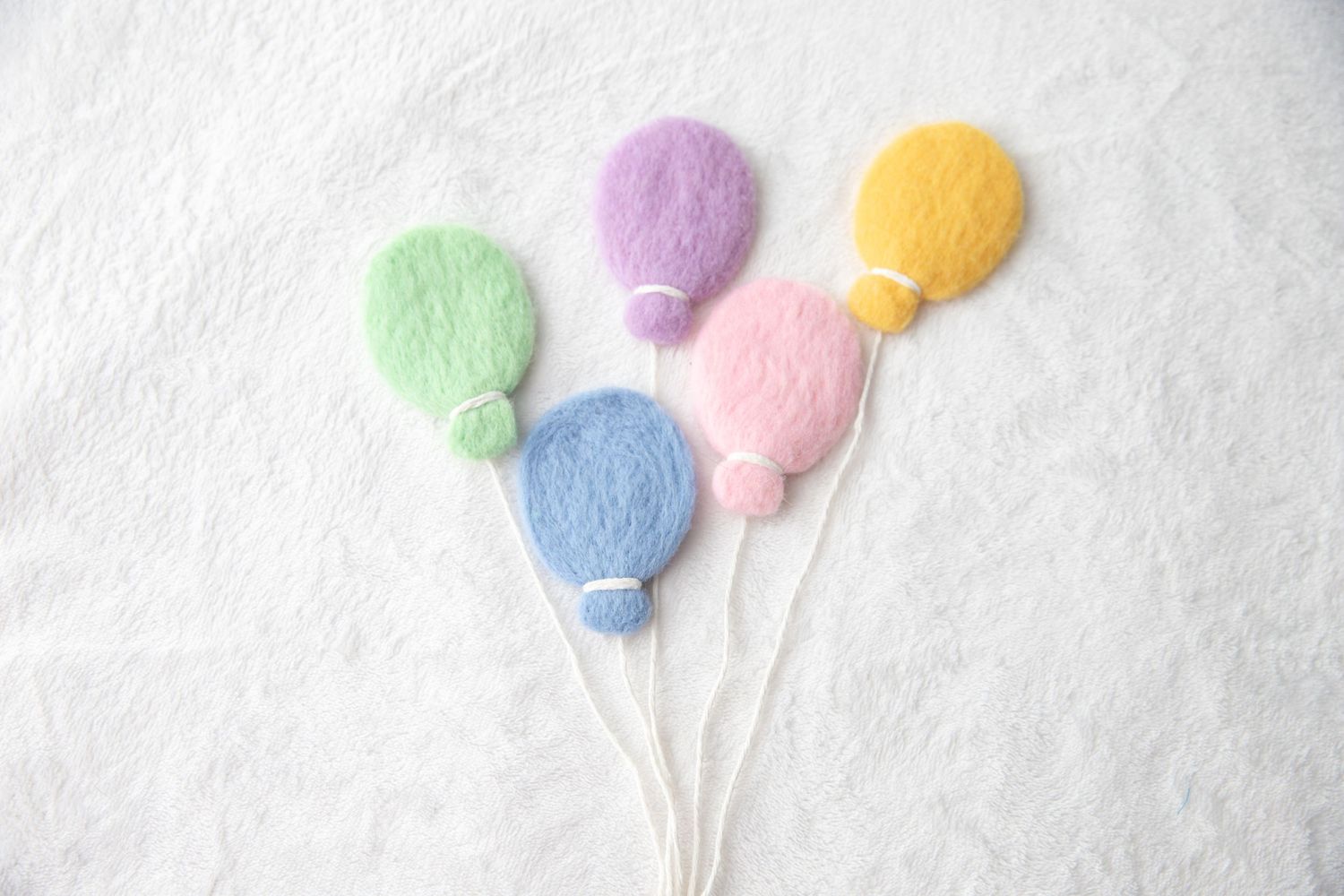 Five pastel felt balloons in green, blue, pink, purple and yellow on white background.