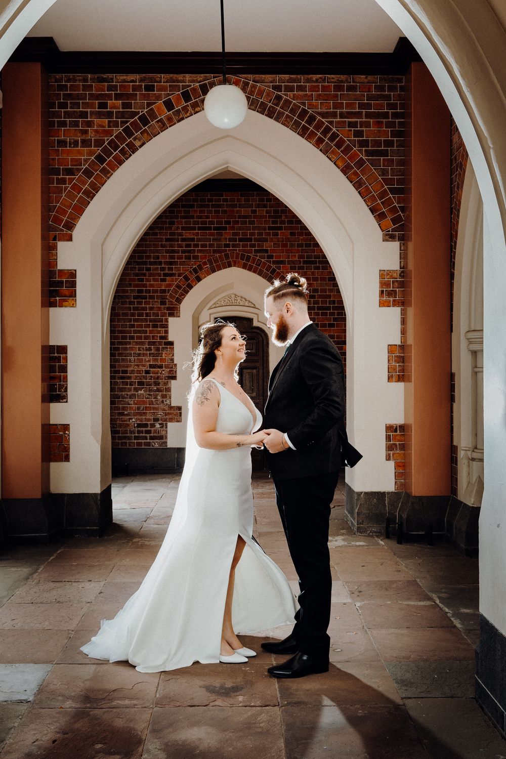 A couple stands together under an elegant brick archway, captured by Apertured Media Auckland Wedding Photographer.