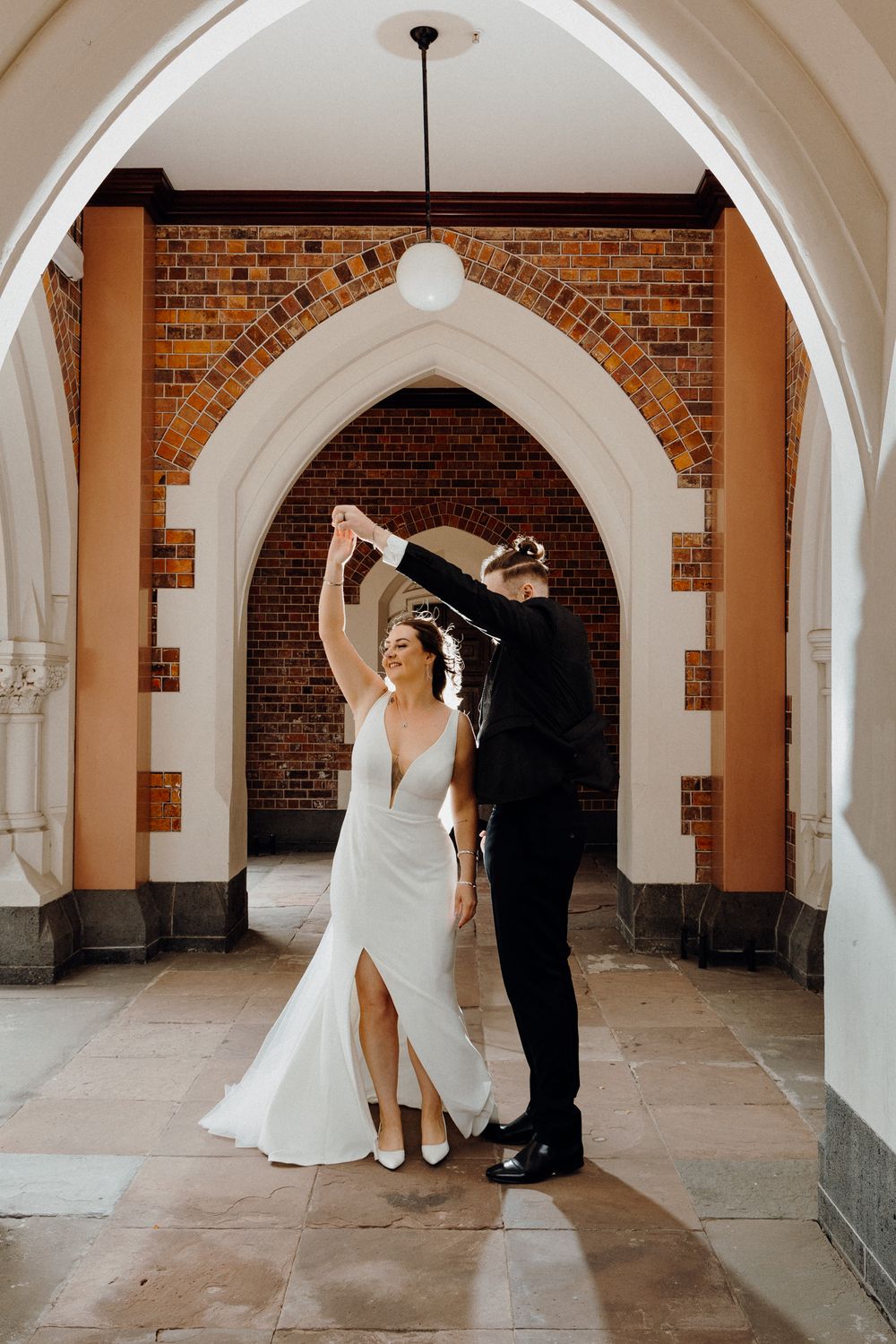 A couple dancing together under an elegant brick archway in a historic building, captured by Apertured Media Auckland Wedding Photographer.