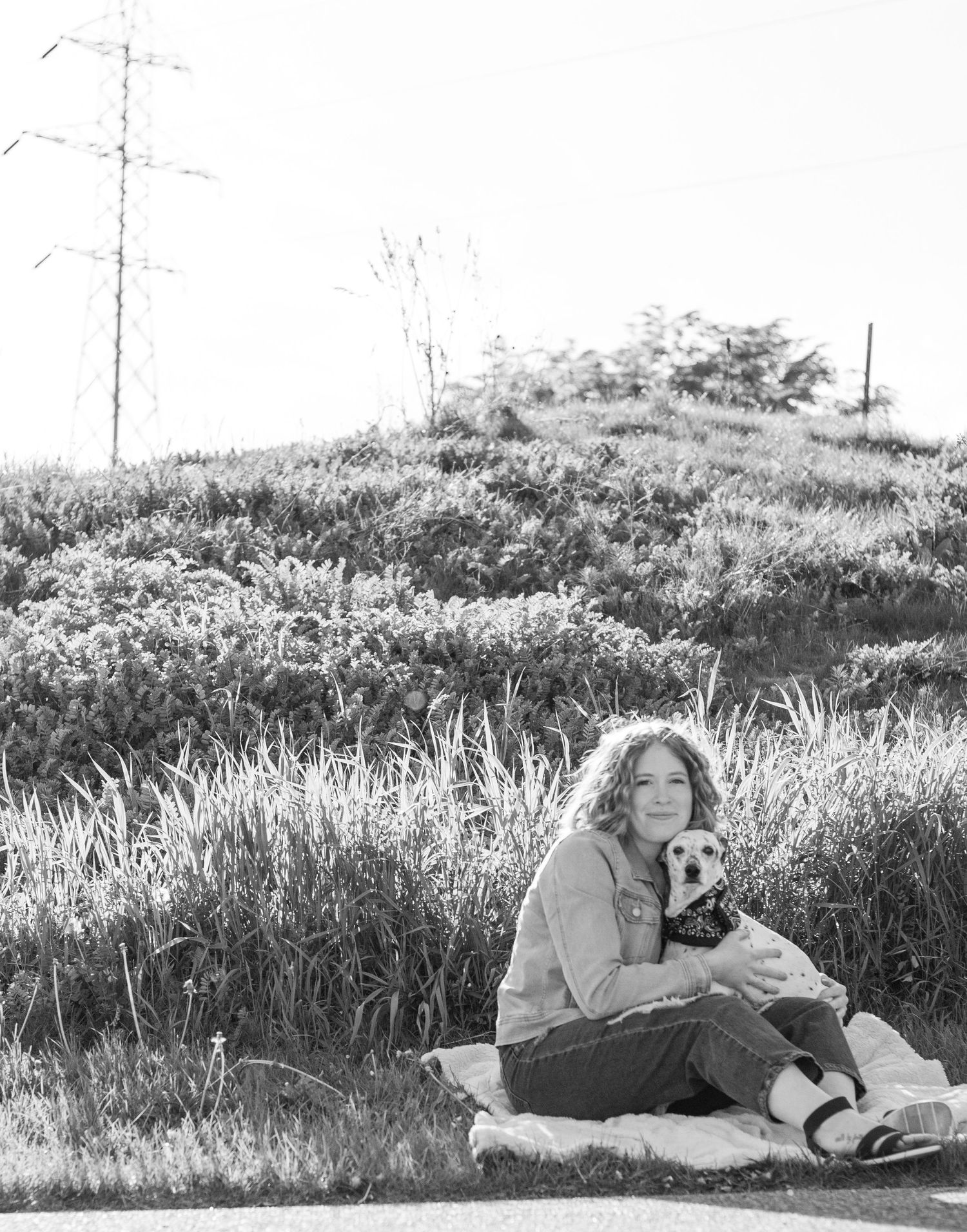 Person sitting on grassy hillside with small dog in black and white photograph.