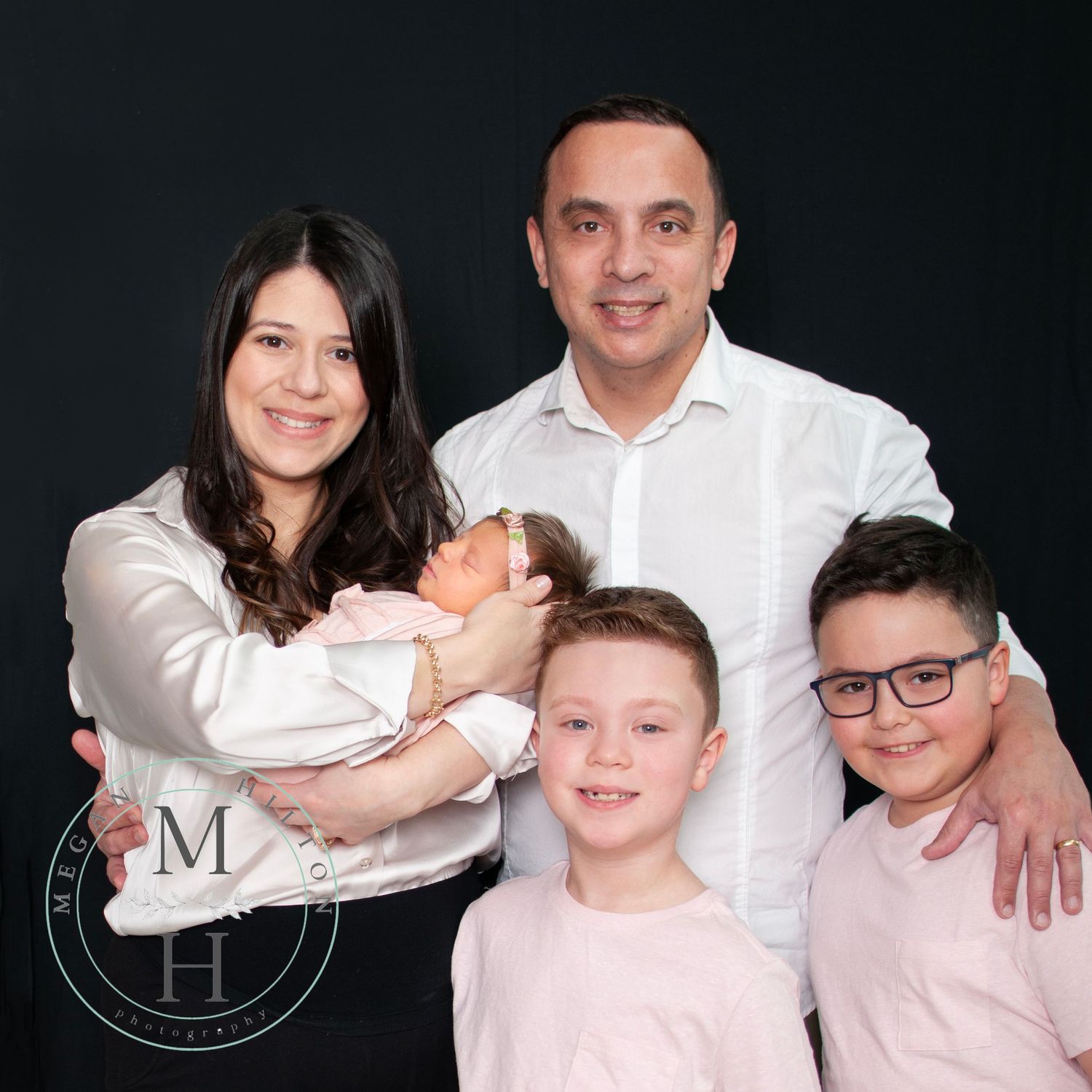 A family of five with newborn baby girl and two older boys on a black backdrop