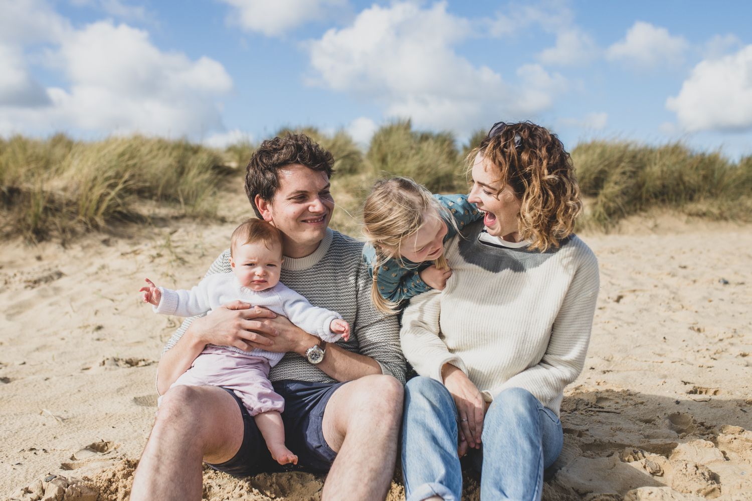 Family enjoying a sunny day together on sandy beach dunes.