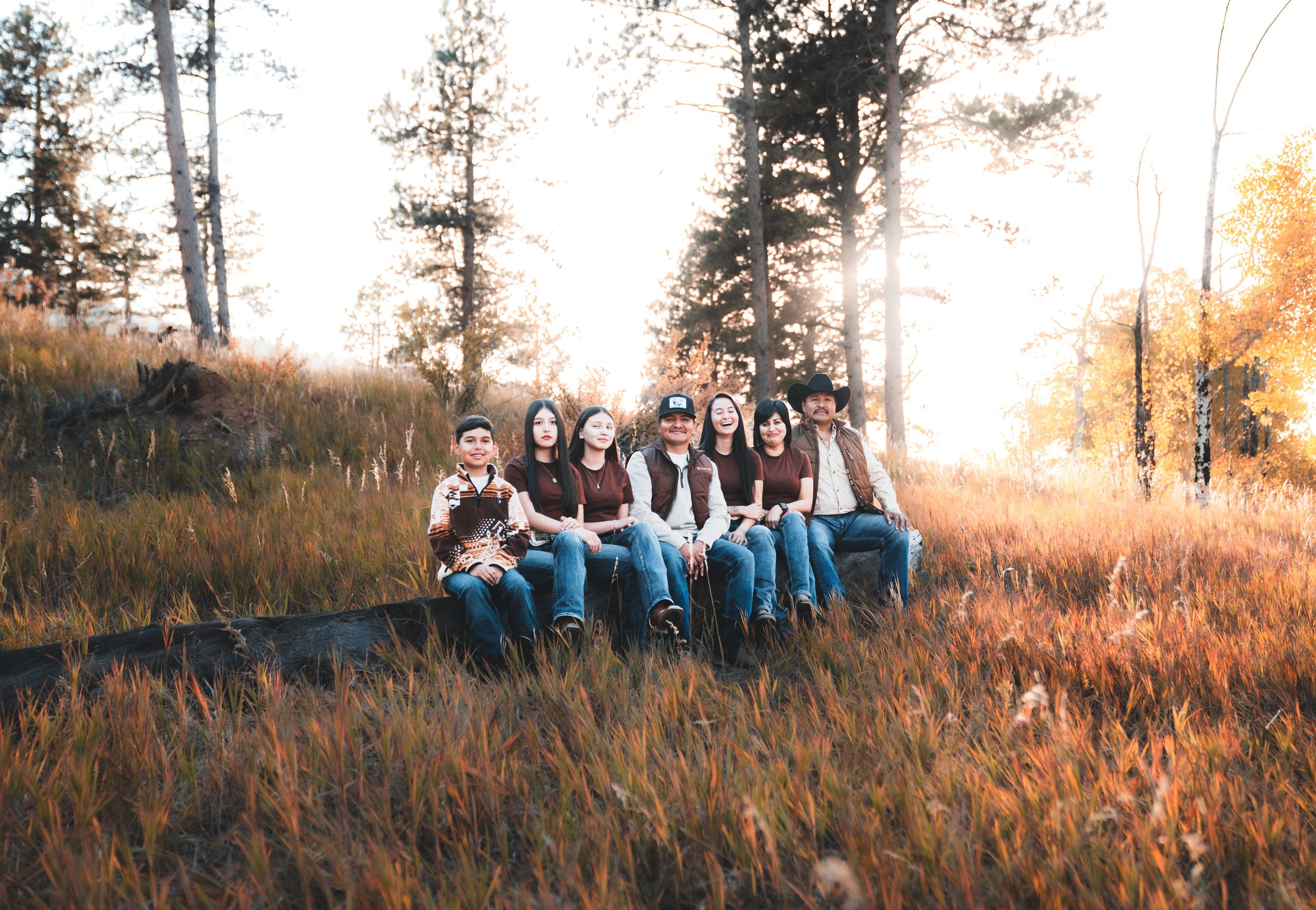 A group stands together in a golden autumn field with tall grass and evergreen trees at sunset.