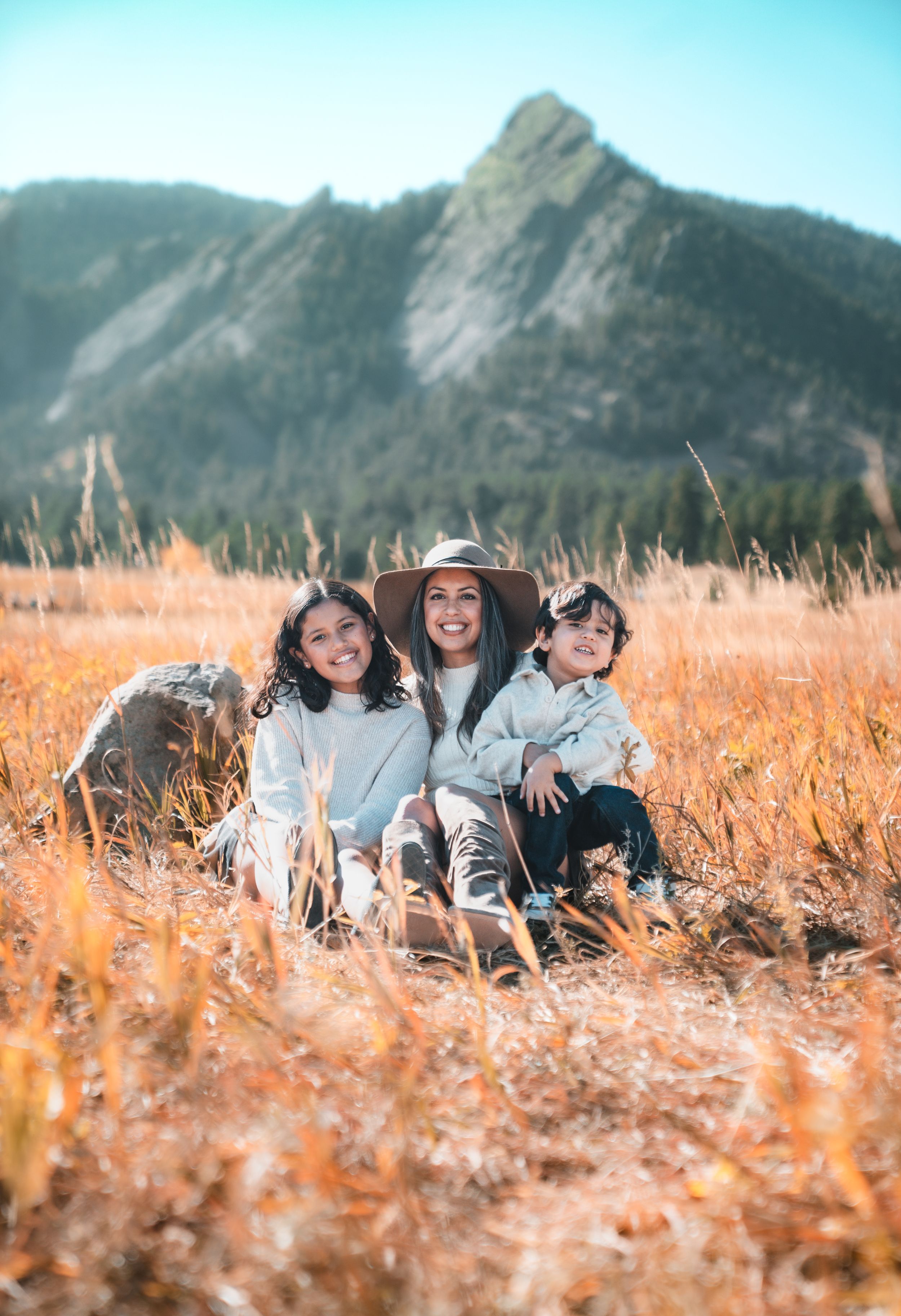 Group sitting together in golden autumn field with mountains in background creating joyful outdoor scene.