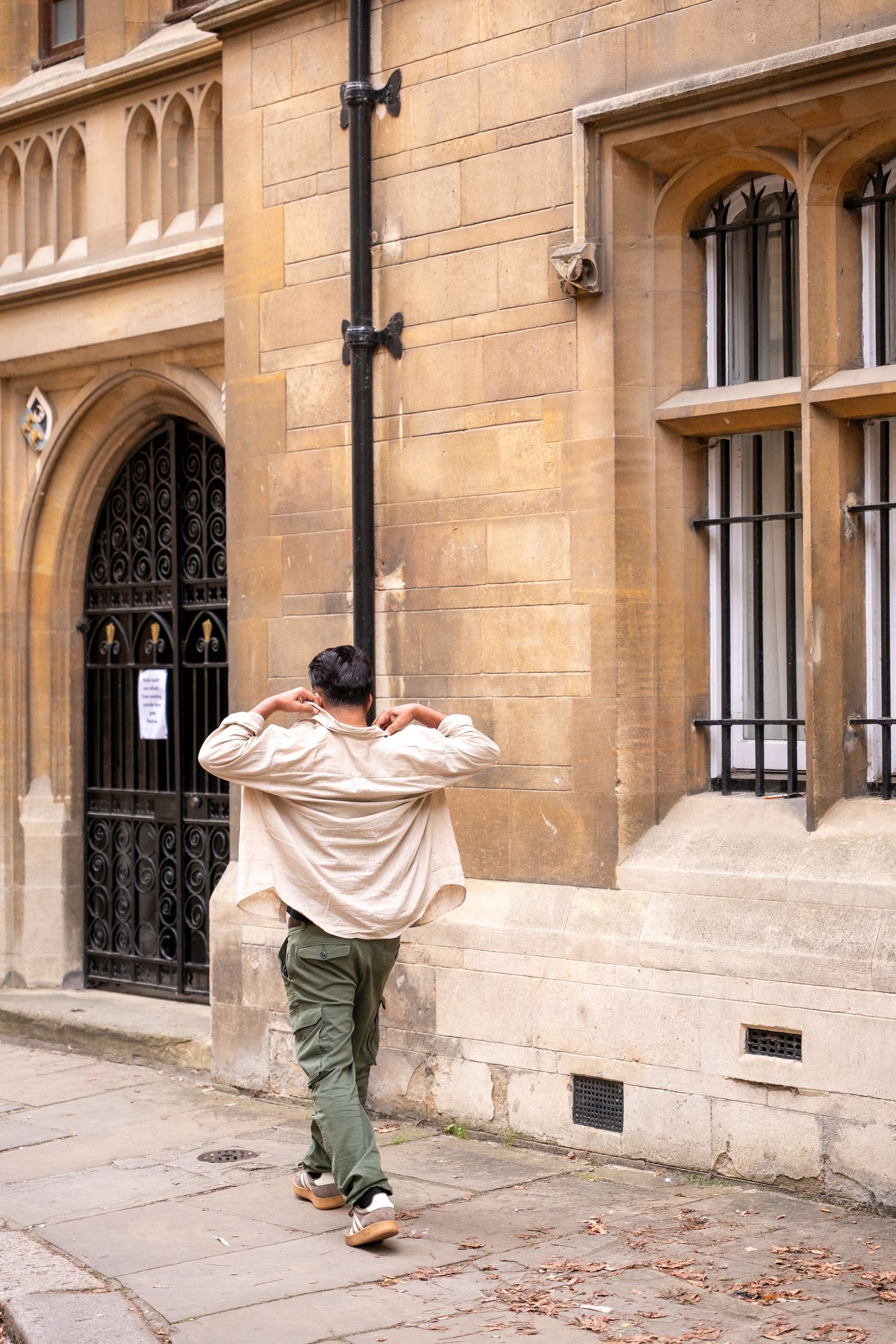 Person in casual attire stands against a stone building with Gothic architectural features and arched doorway.