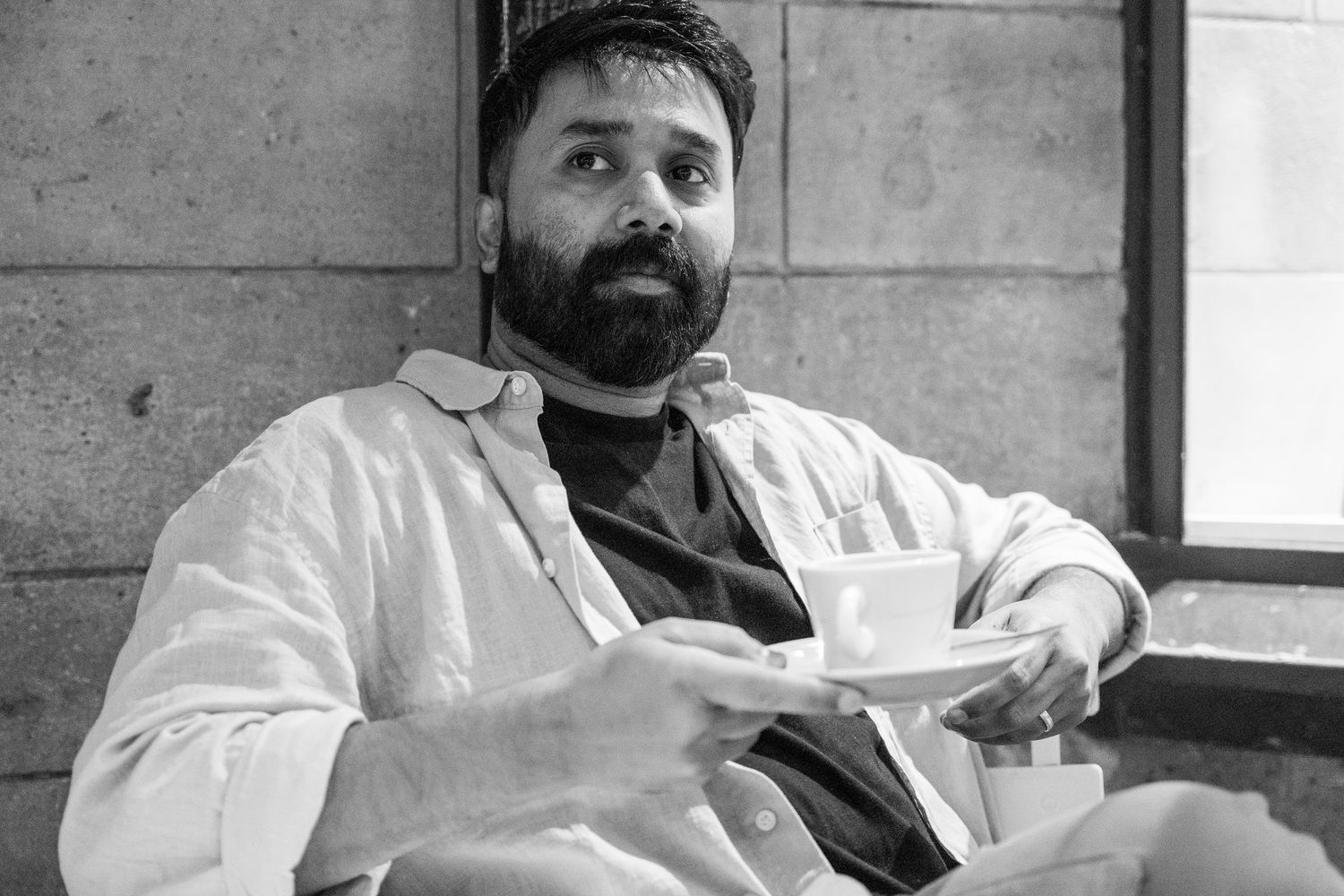 Black and white photo of person in white shirt sitting casually and holding a coffee cup.