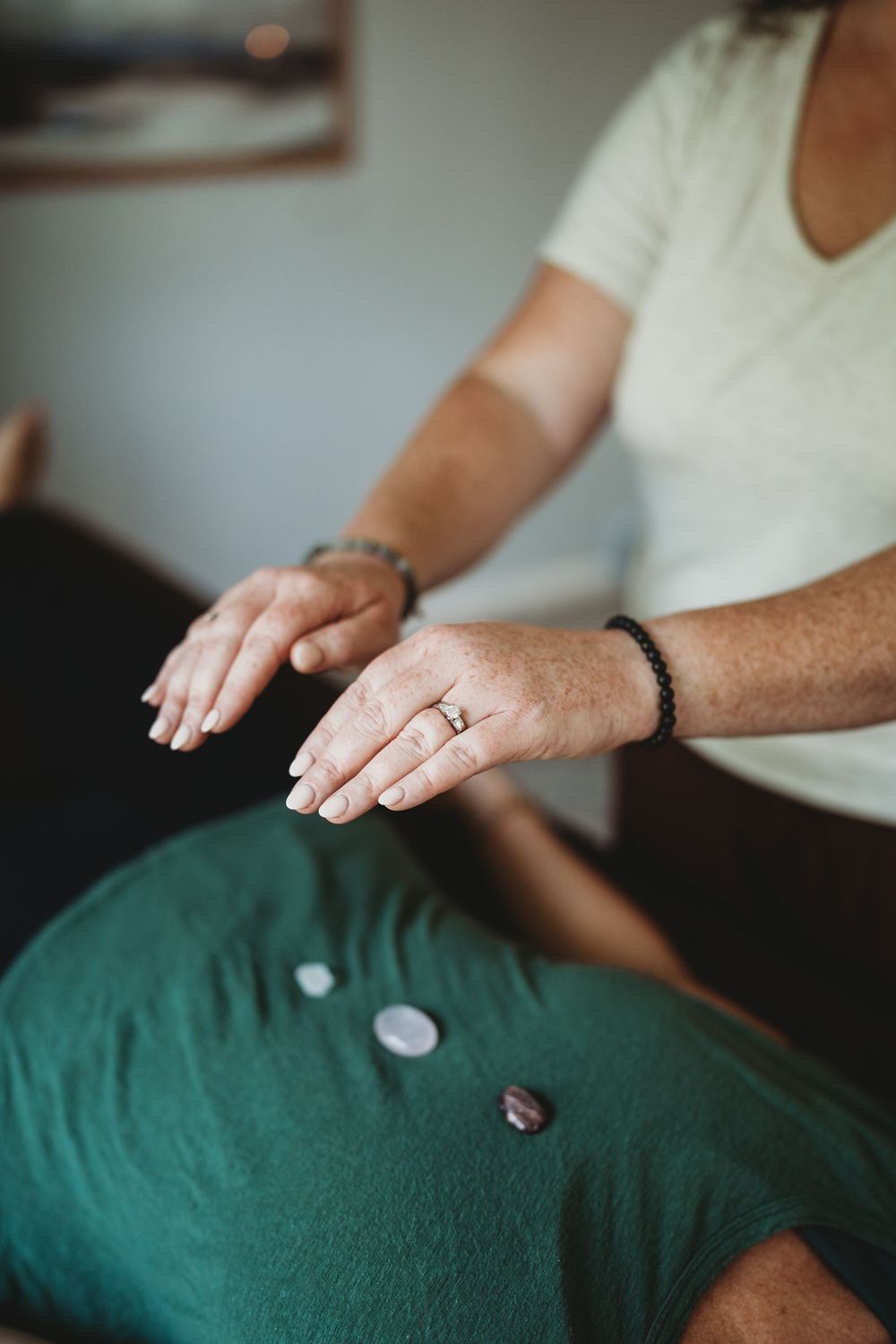Close-up view of hands wearing a wedding ring and bracelet resting on a green cushioned surface.