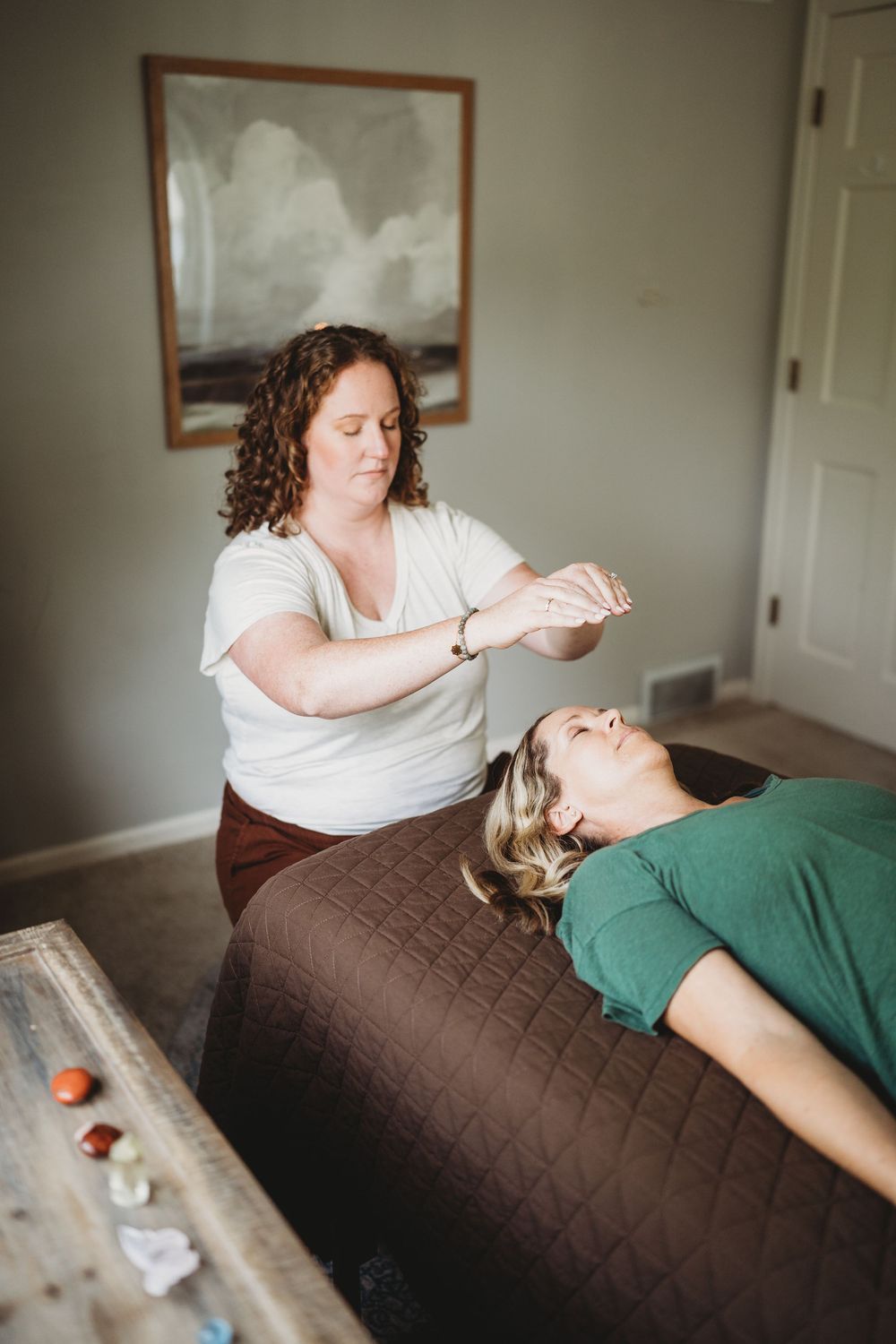 A massage therapist performs a craniosacral therapy treatment on a client lying on a brown massage table.