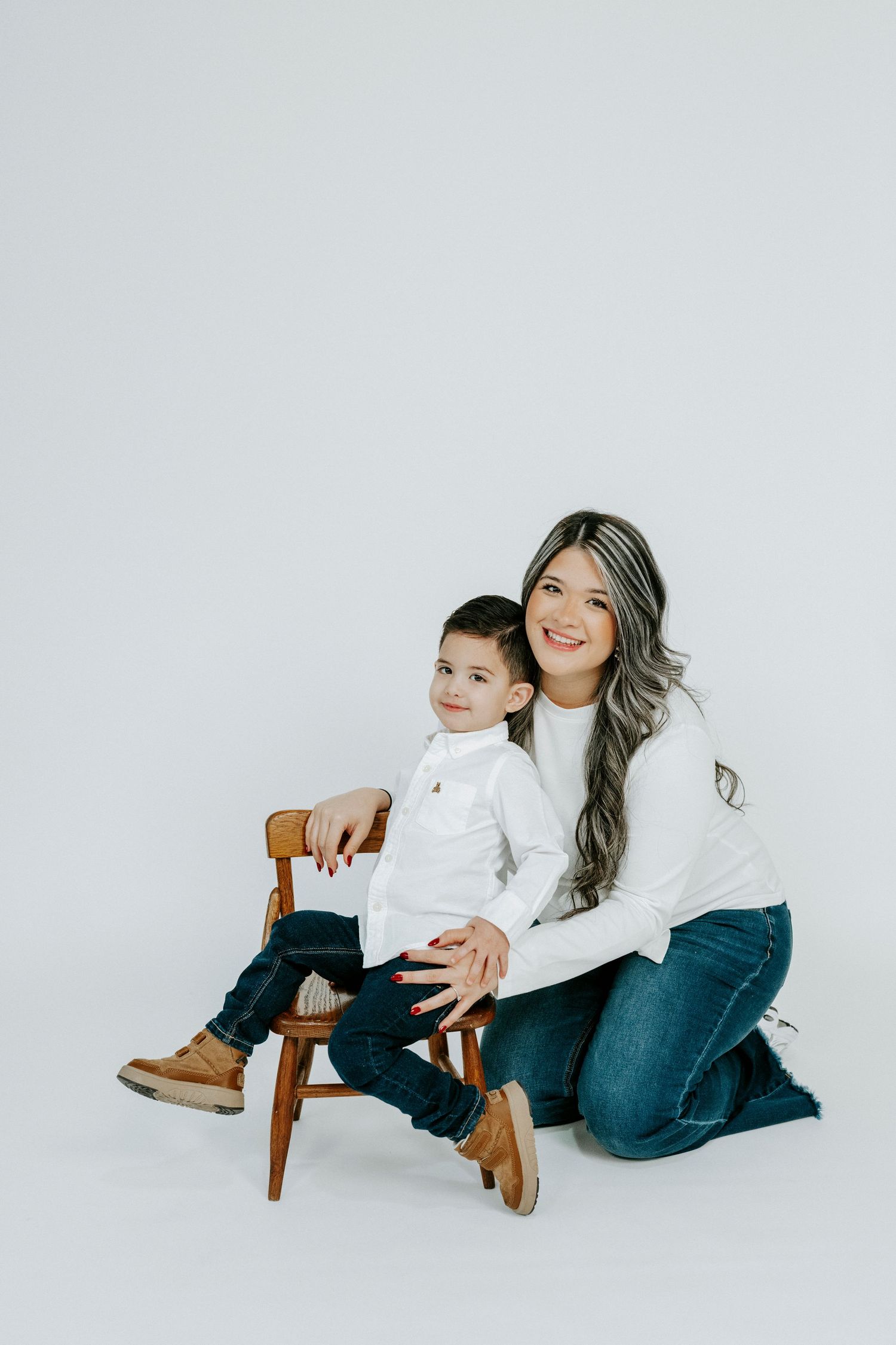 A family in matching white tops and jeans poses playfully on the floor in a minimalist studio setting.