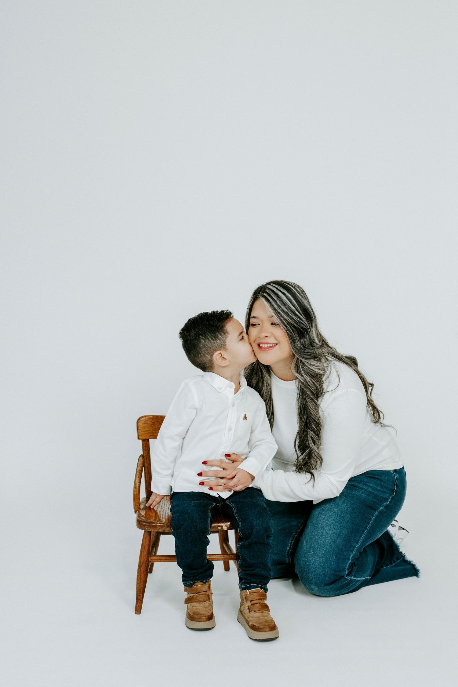 Mother and child share an affectionate moment on a wooden chair against white background.