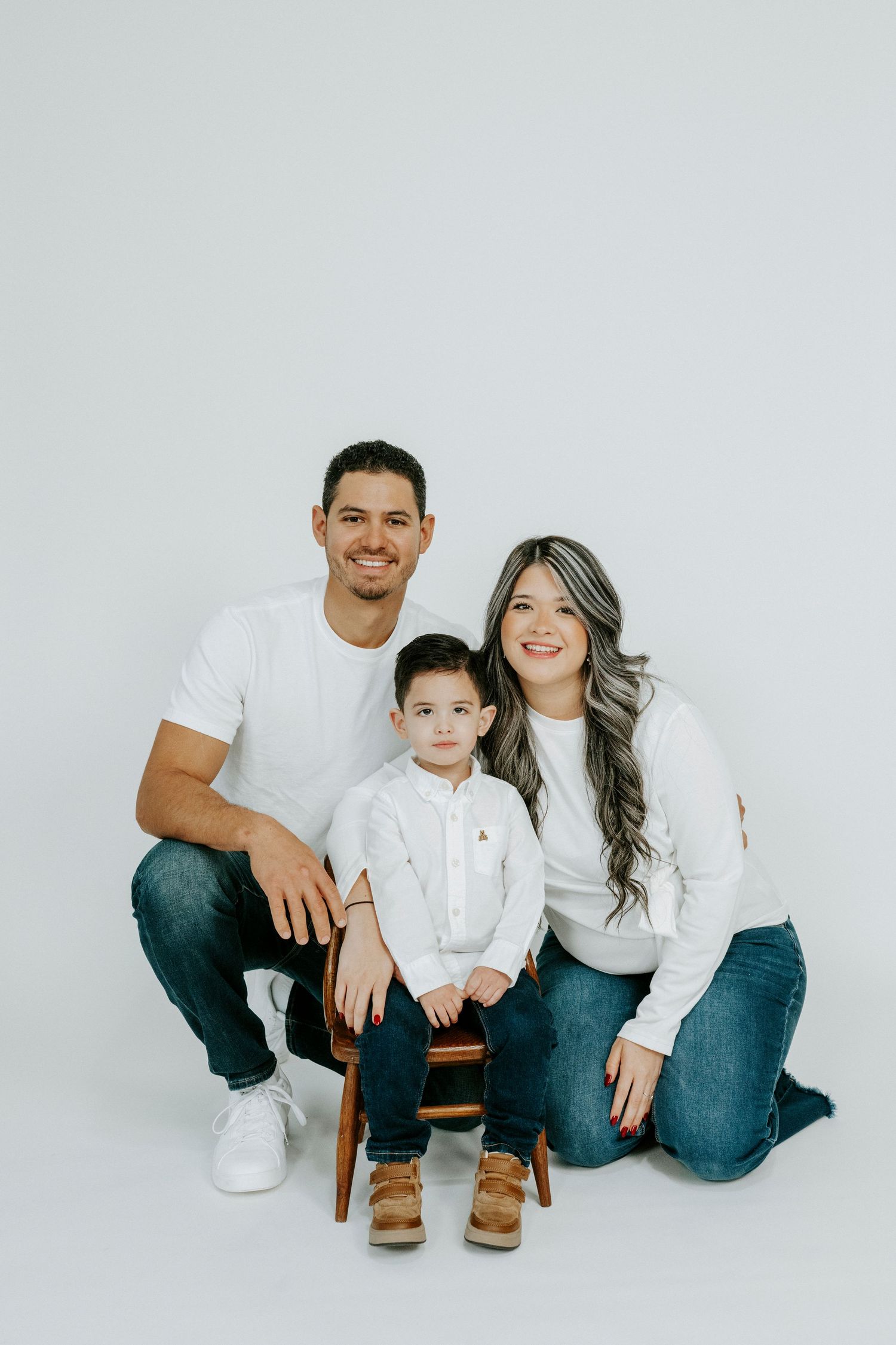 Family wearing coordinated white shirts and blue jeans poses together against white backdrop in studio portraits.