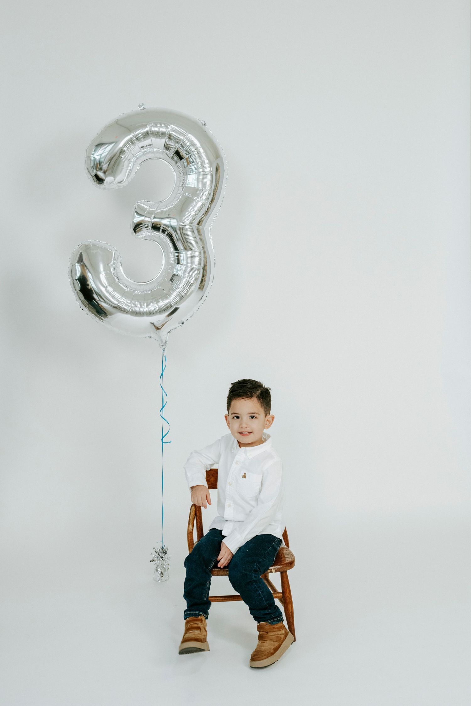 A series of minimalist photos showing a white chair against a gray background with a silver number 3 balloon.