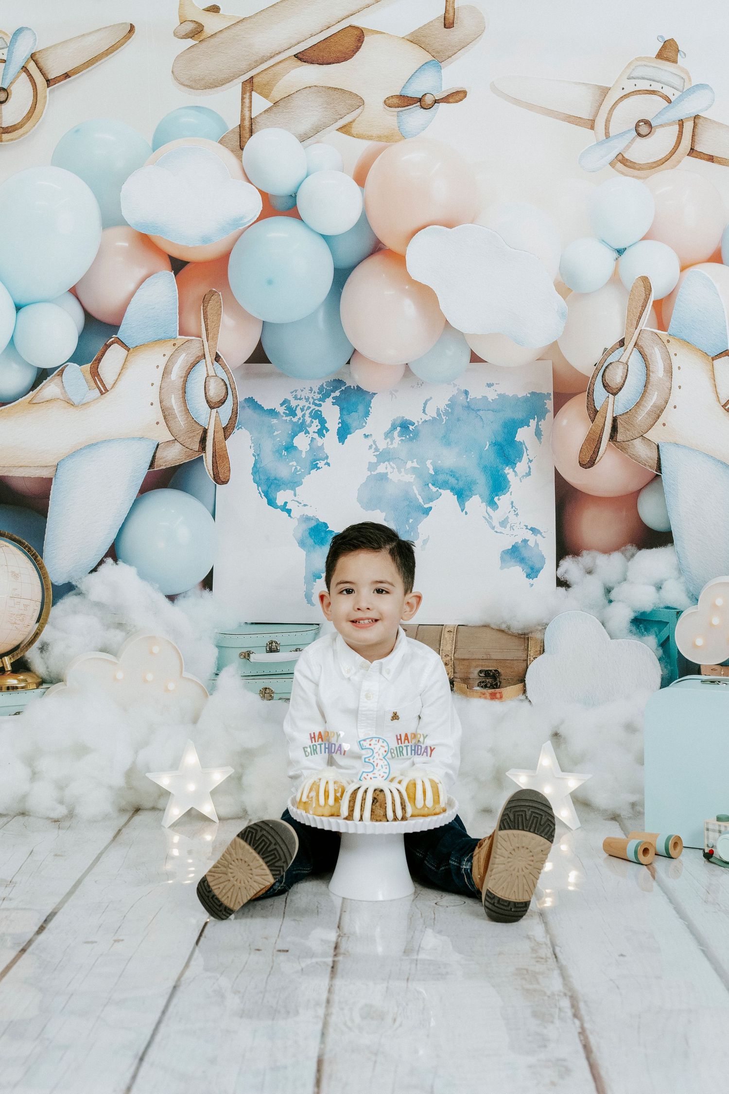 Birthday setup with white and blue balloons, stars, and a cake against a rustic wood floor background.