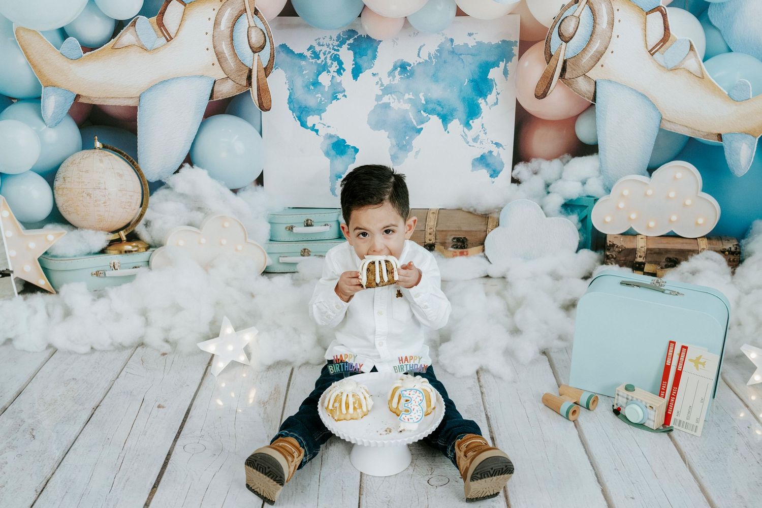 A small baby lies on a wooden floor surrounded by white cotton balls and soft blue decorative elements.