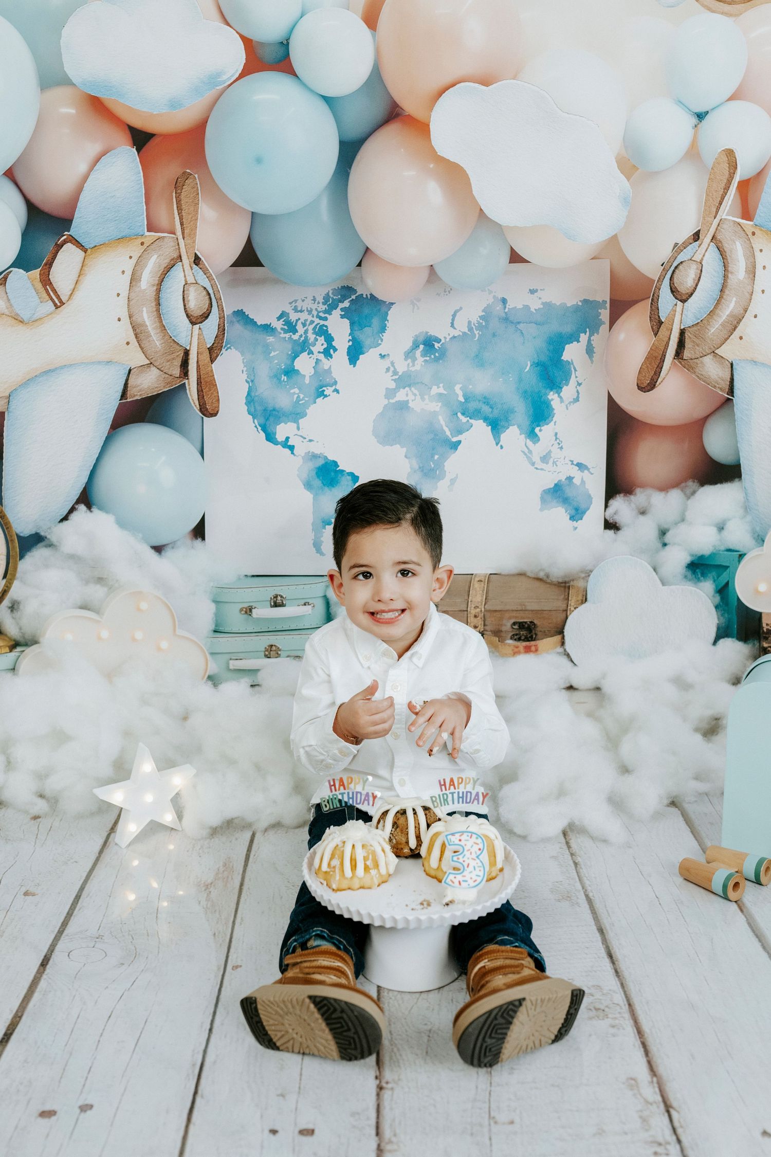 Birthday setup with blue and peach balloons, cotton clouds, and stars on white wooden floor.