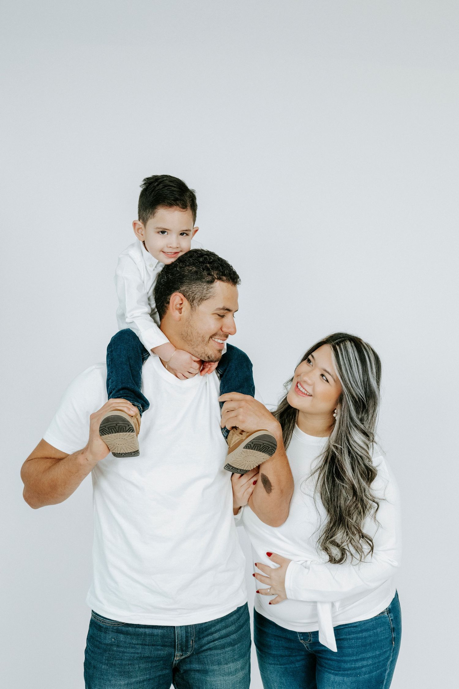 Family wearing coordinated white shirts and jeans share joyful moments against a white background.