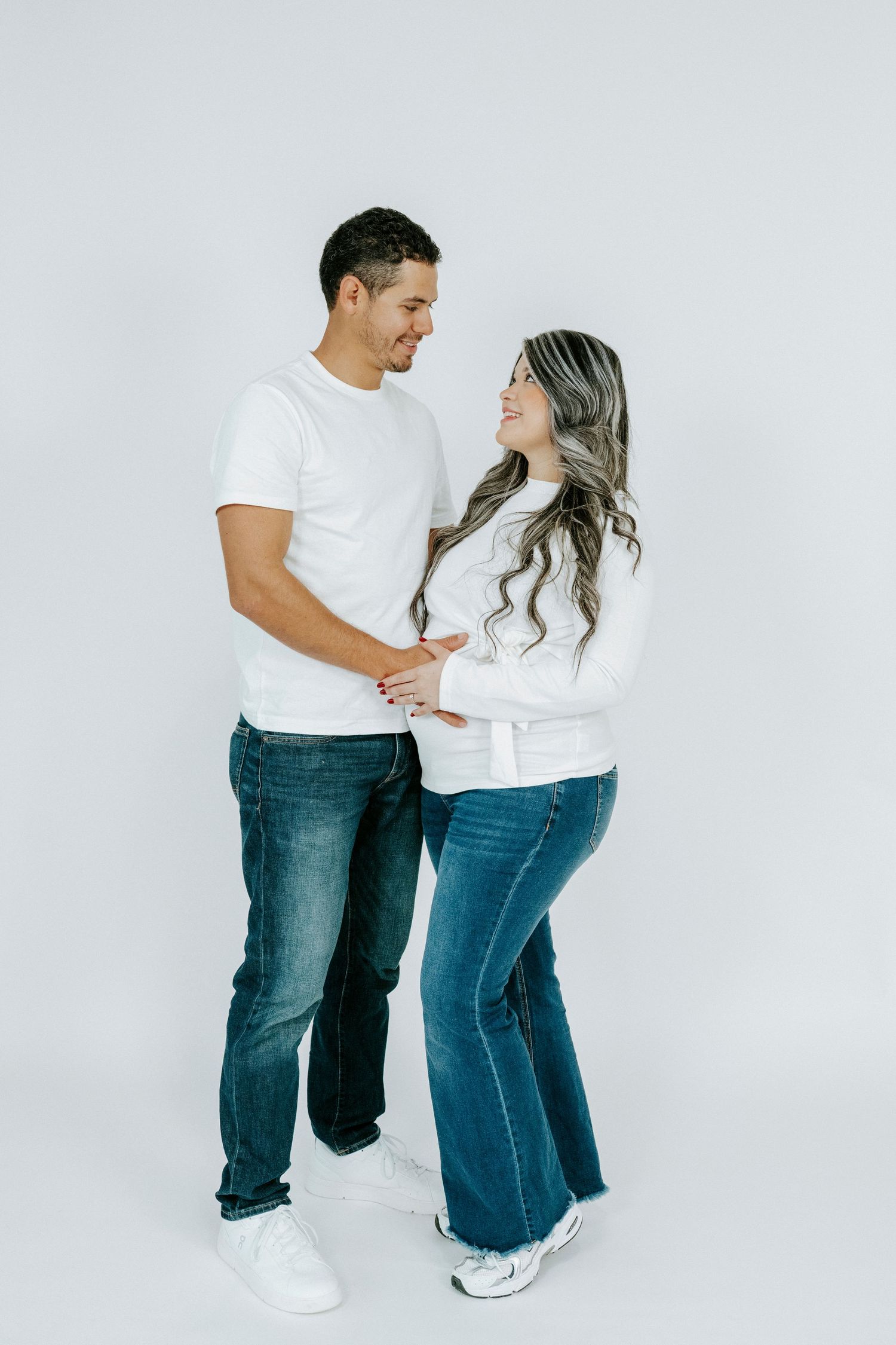 Couple in matching white tops and jeans pose playfully against white background.