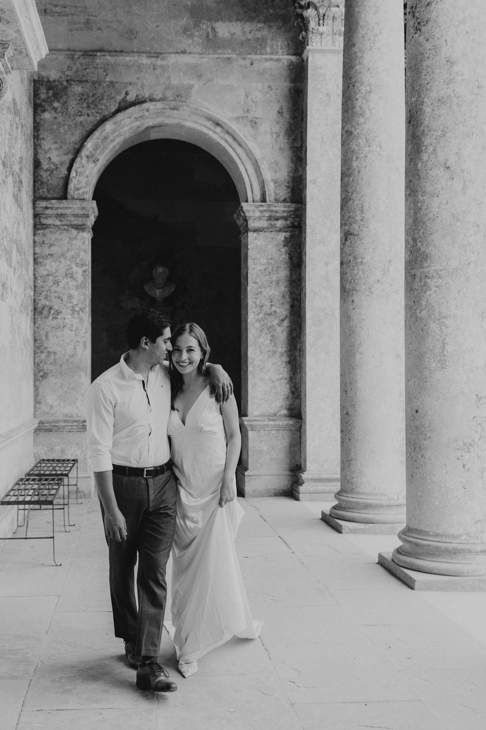 Relaxed engagement couple walking under stone arches at Stourhead National Trust