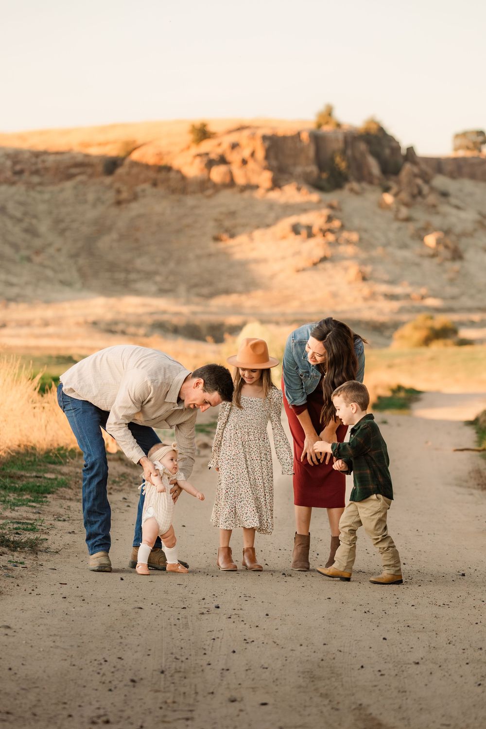 A group bends down to examine something interesting on a sandy beach at sunset.