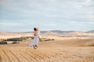 Rolling hills and harvested wheat fields stretch across a vast rural landscape under cloudy skies.