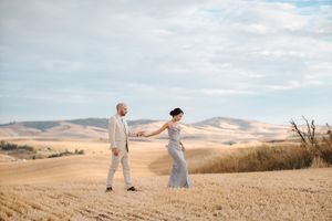Two figures in light clothing dance together across rolling golden hills under a cloudy sky.