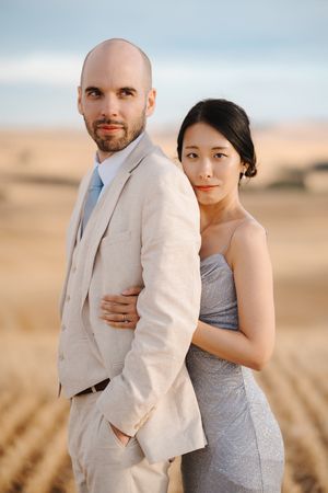 Couple embracing in a golden wheat field at sunset with mountains in the distance.