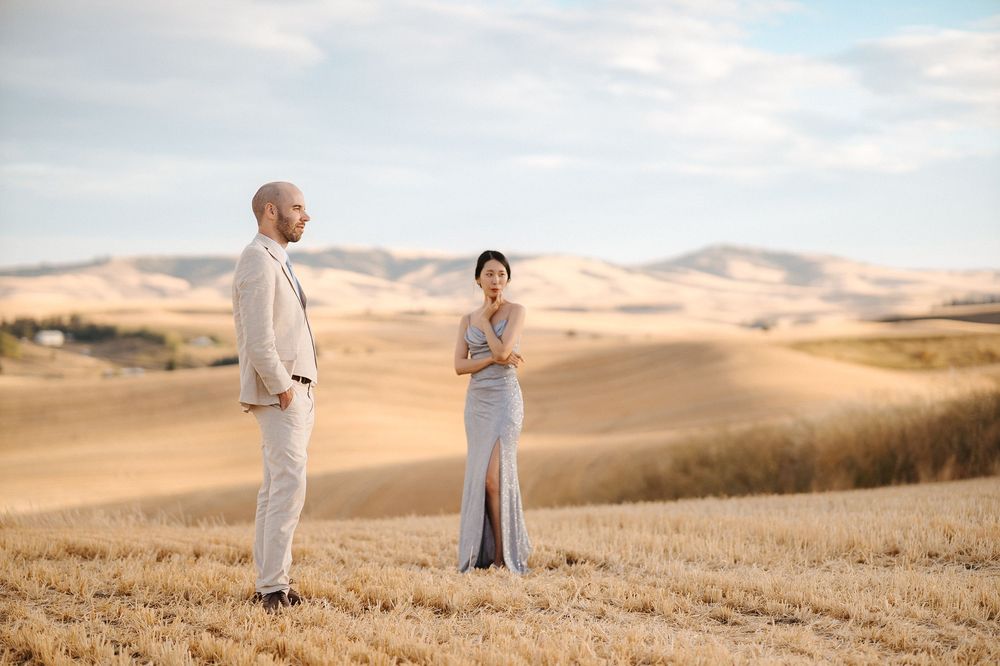 Romantic couple stands together in distance across rolling desert hills during golden hour.