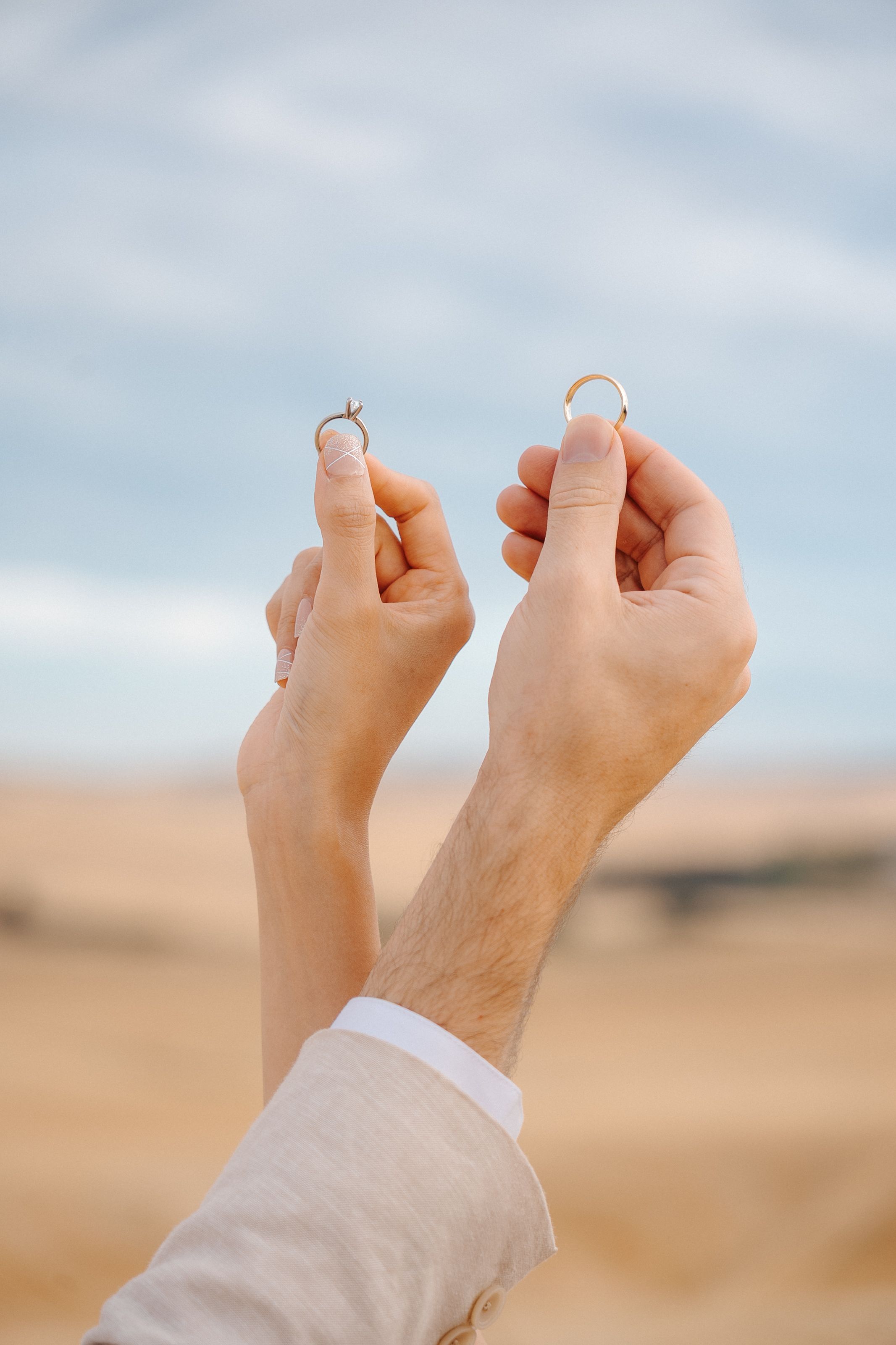 Close-up of hands holding wedding rings against a blurred desert landscape background.