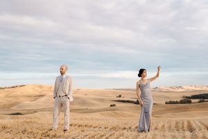 A couple in coordinated outfits twirls and dances through a sun-drenched wheat field at sunset.