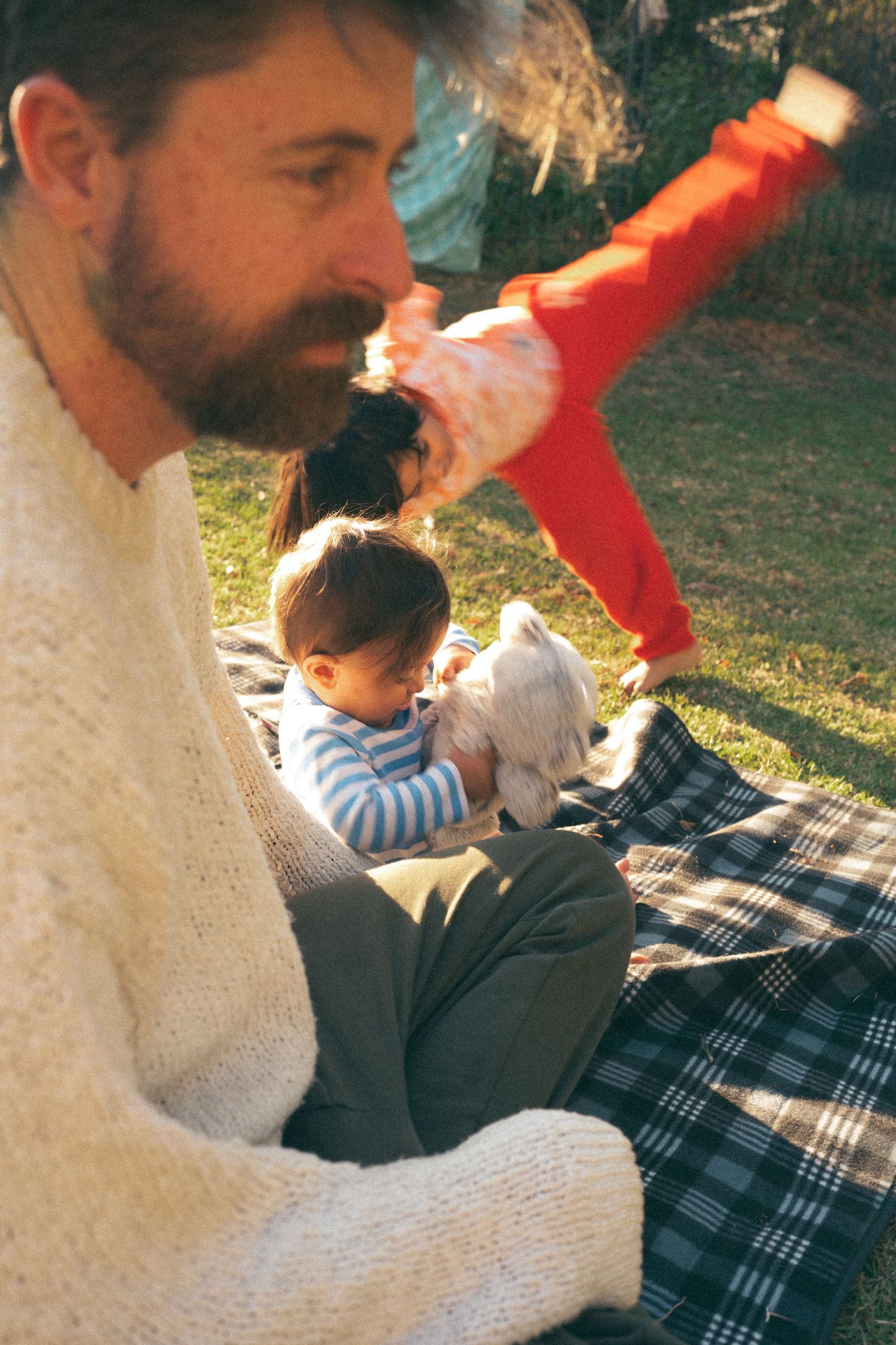 Family relaxing on picnic blanket in park during golden hour.