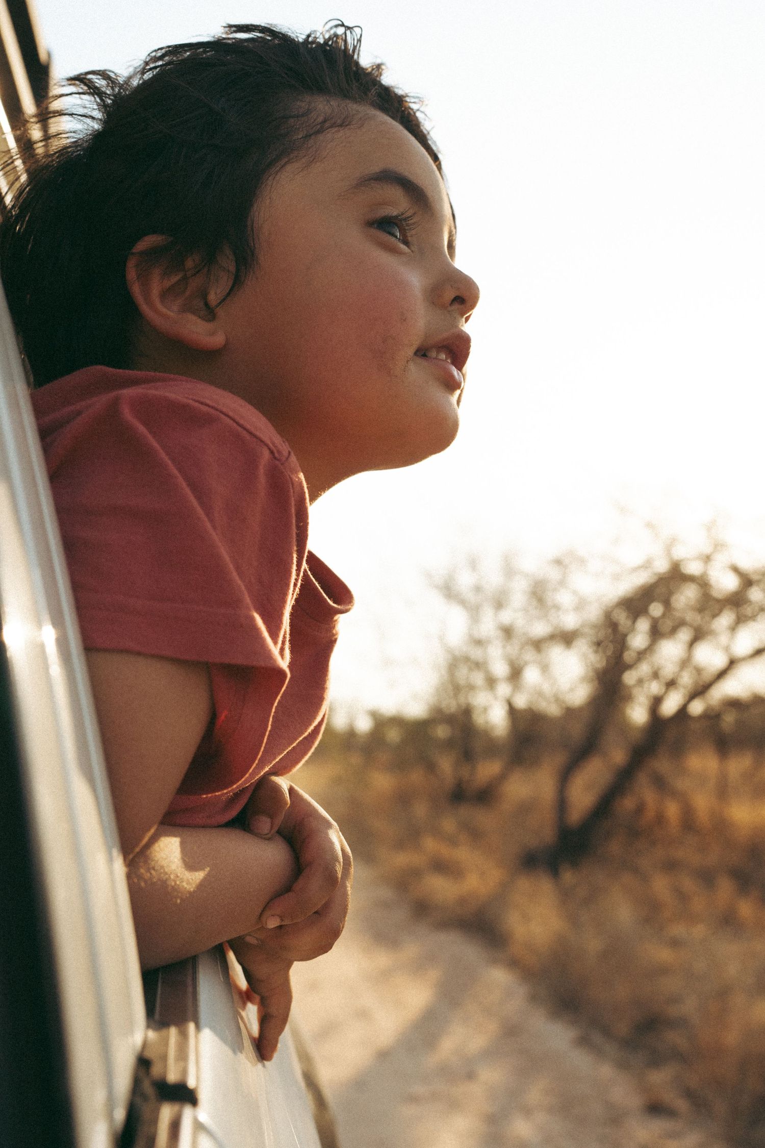 Child looking up through car window during sunset.