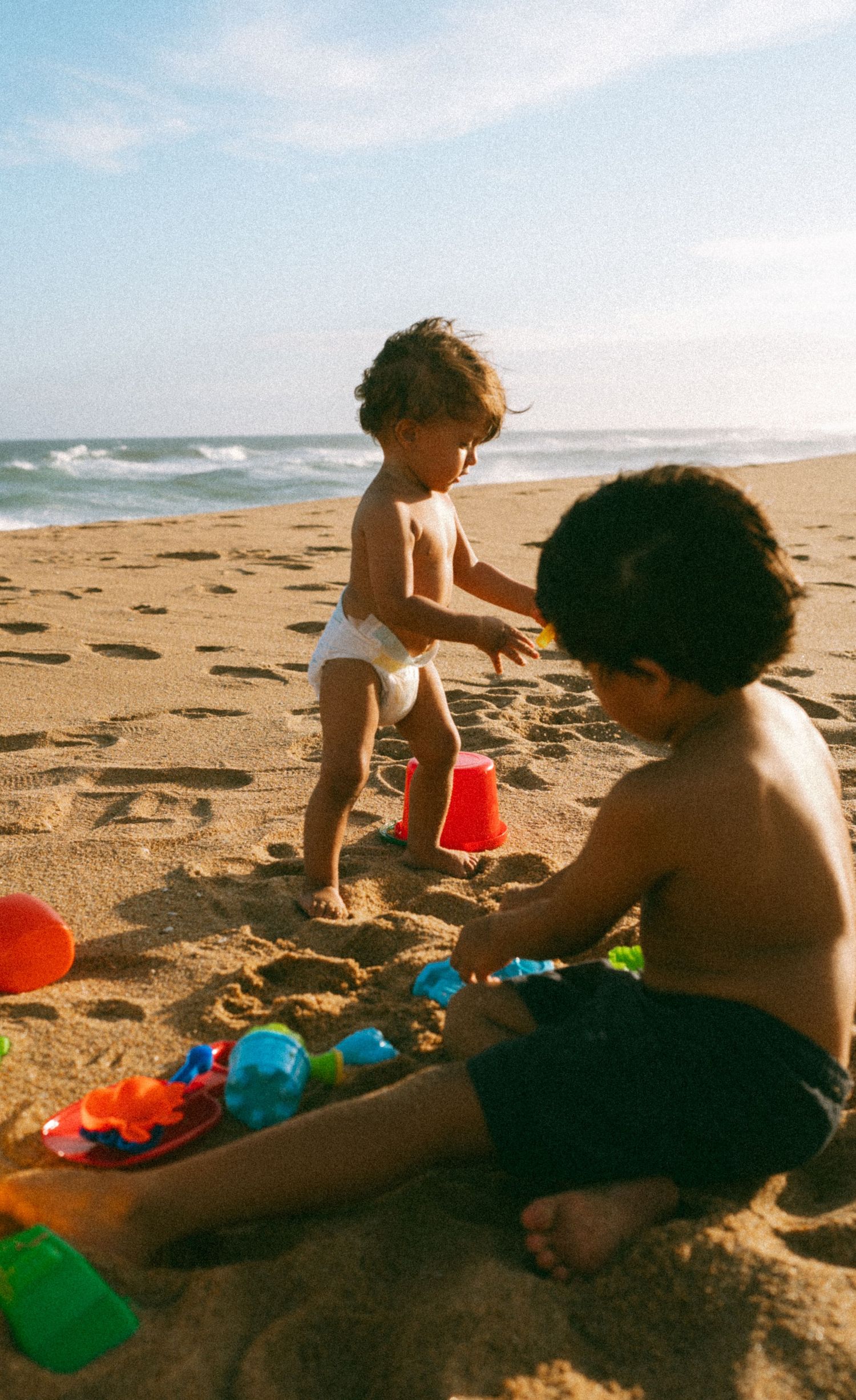 Children playing with beach toys in golden sunlight on sandy shore.