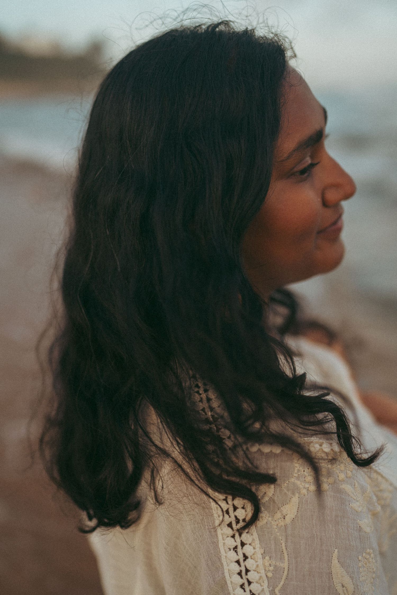 Profile view of woman with flowing dark hair at beach during sunset.