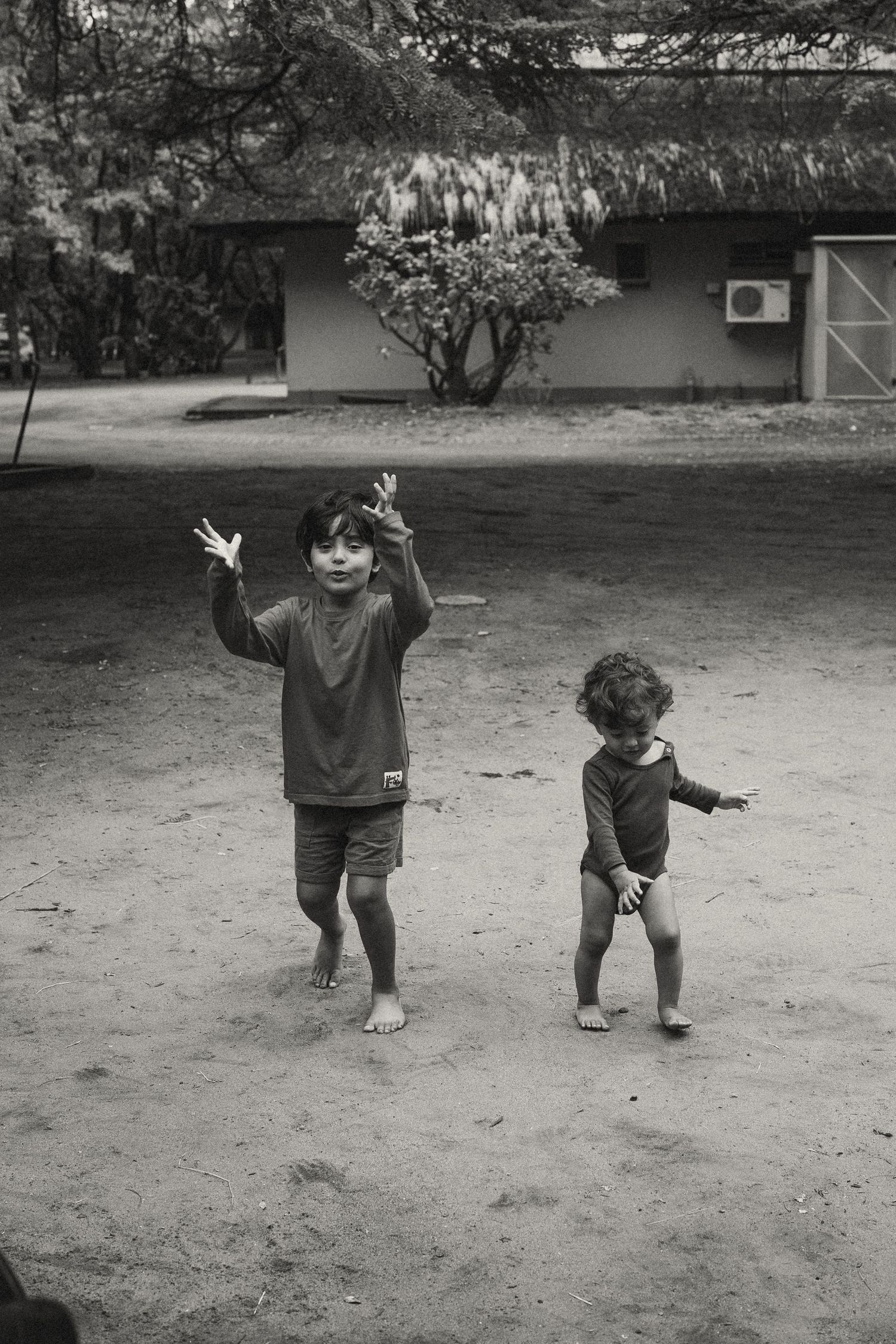 Black and white sequence of children playing and dancing outdoors on a dirt ground.