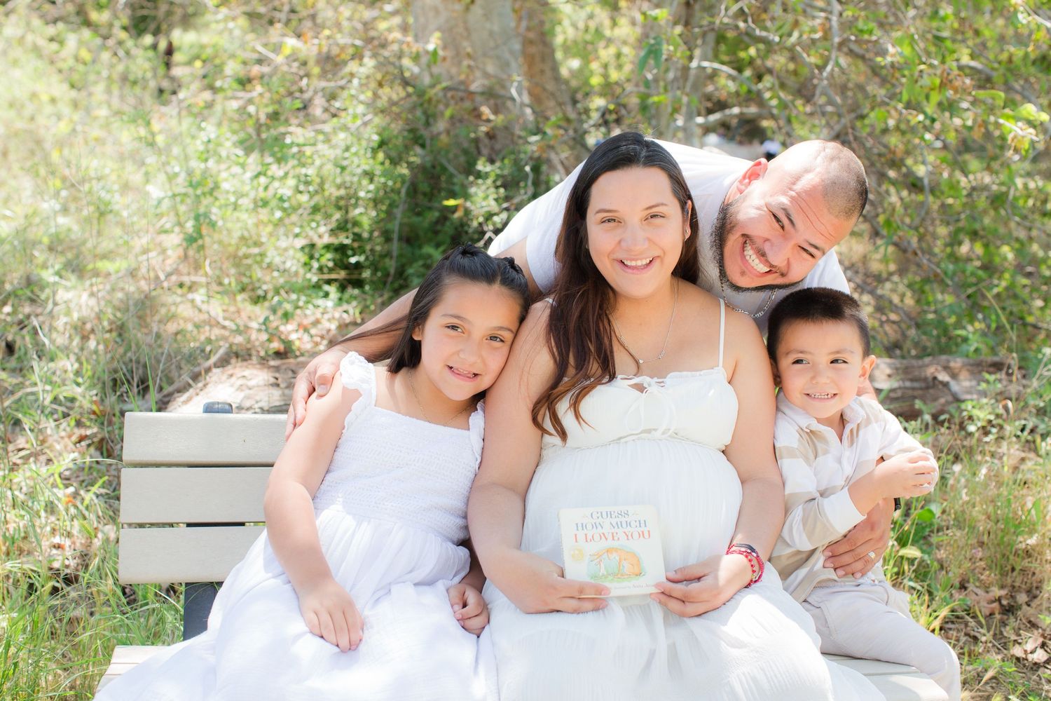Family group portrait session outdoors in white clothing against a natural woodland setting.