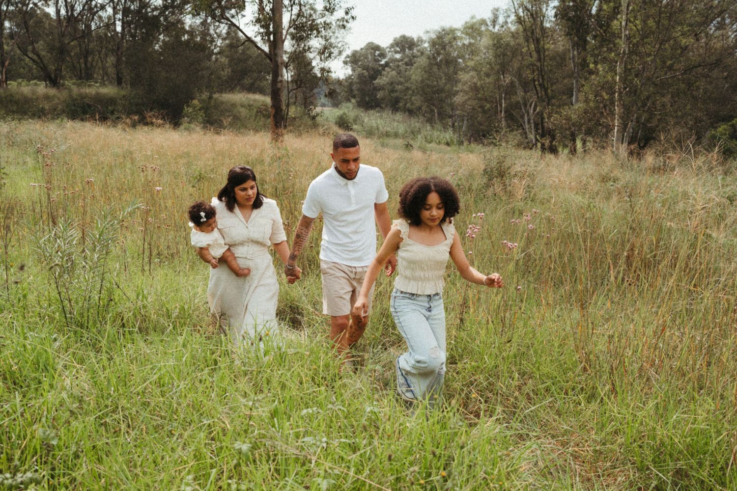 Family walking together through tall grass in a sunlit meadow.