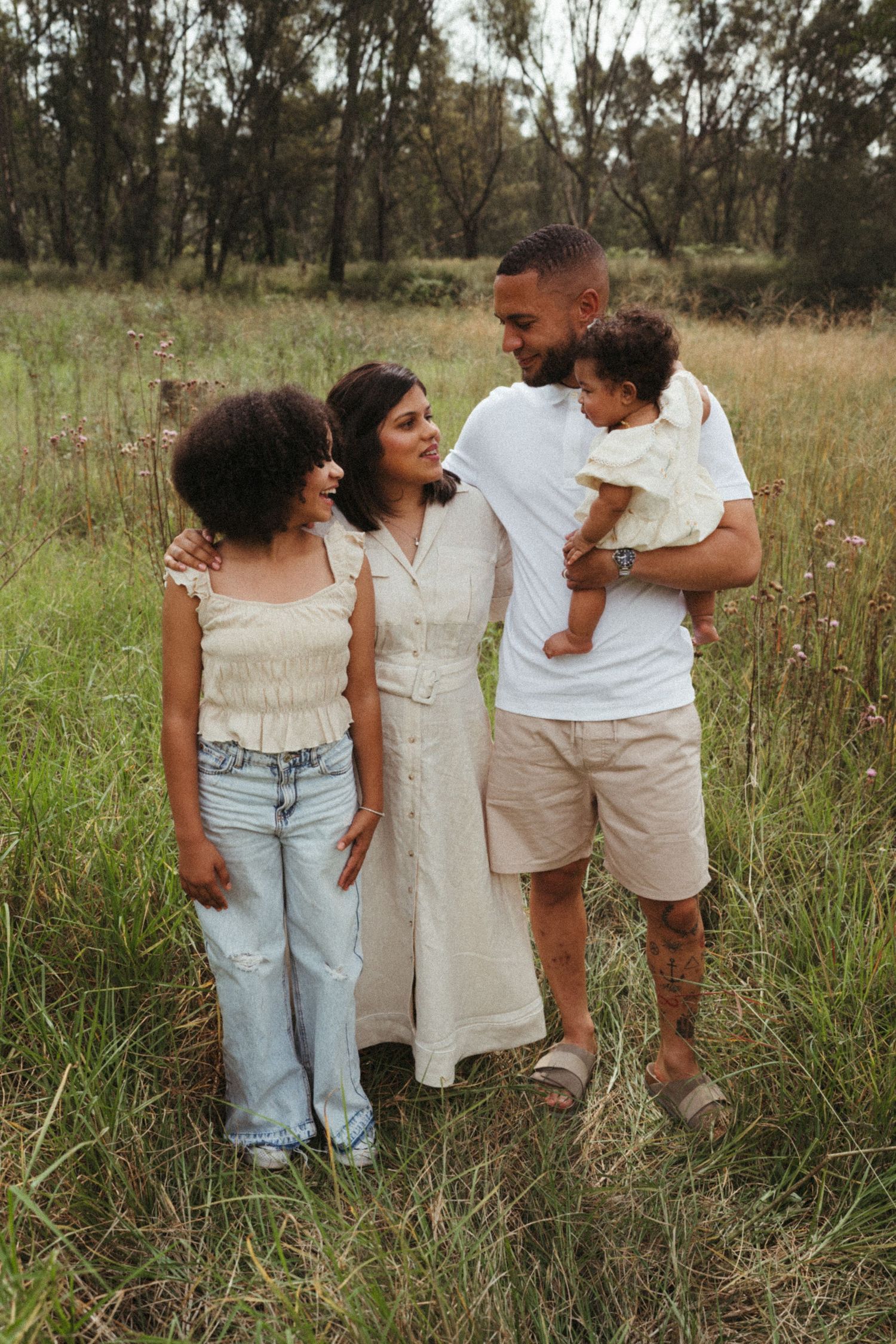 Group in coordinated white and beige outfits poses together in a rustic field setting.