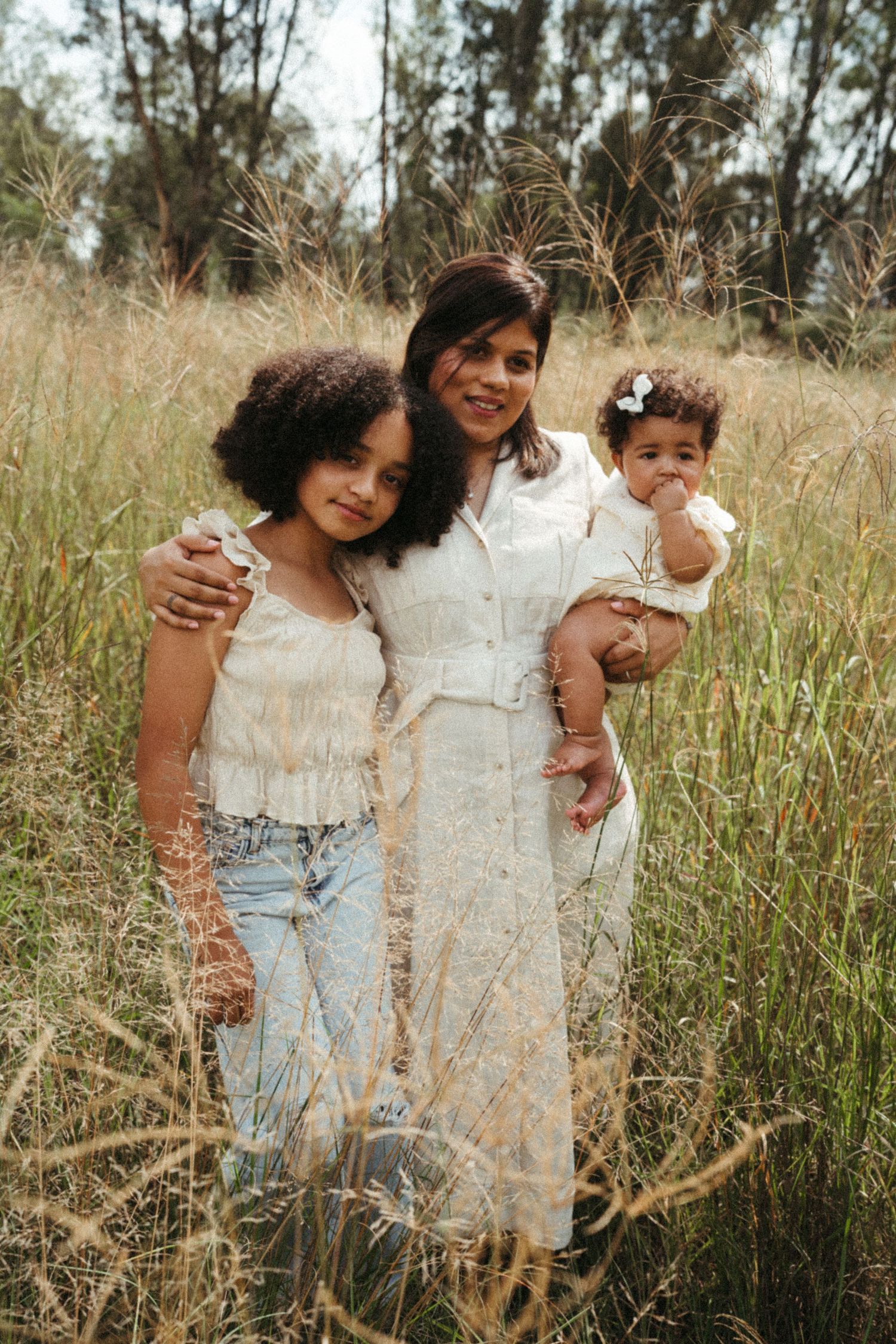 Family members share tender moments while standing in a sunlit meadow.