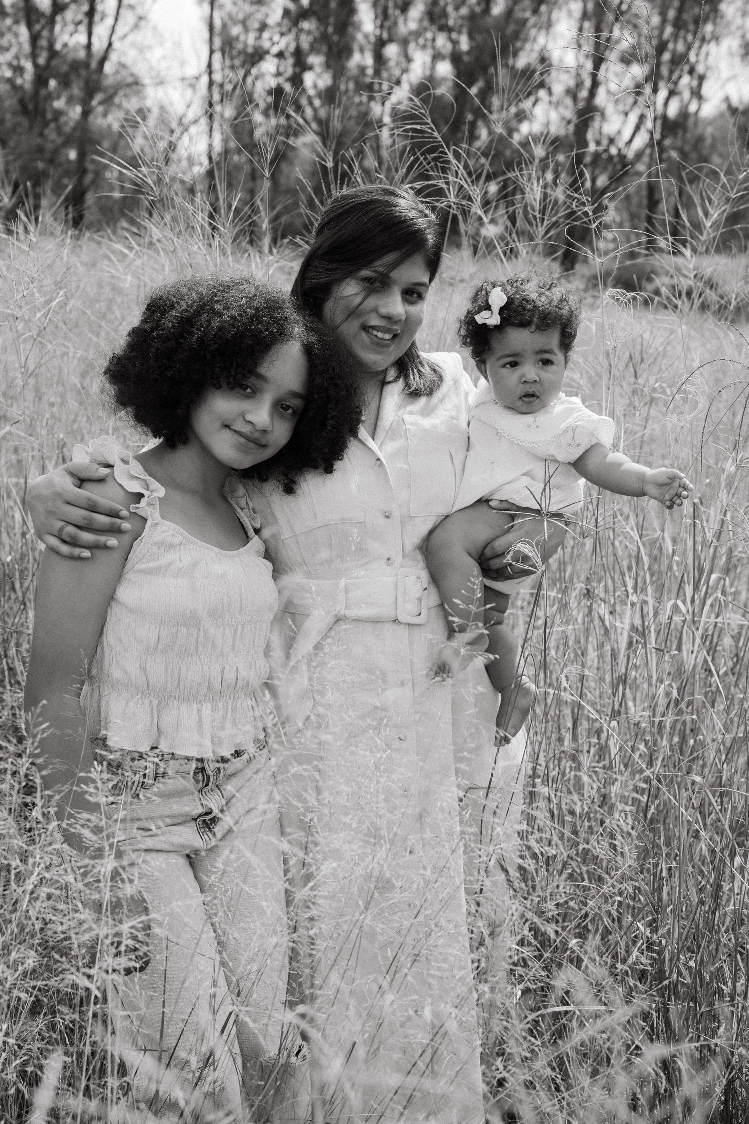 Black and white photo of a family sharing intimate moments in a field of tall grass.