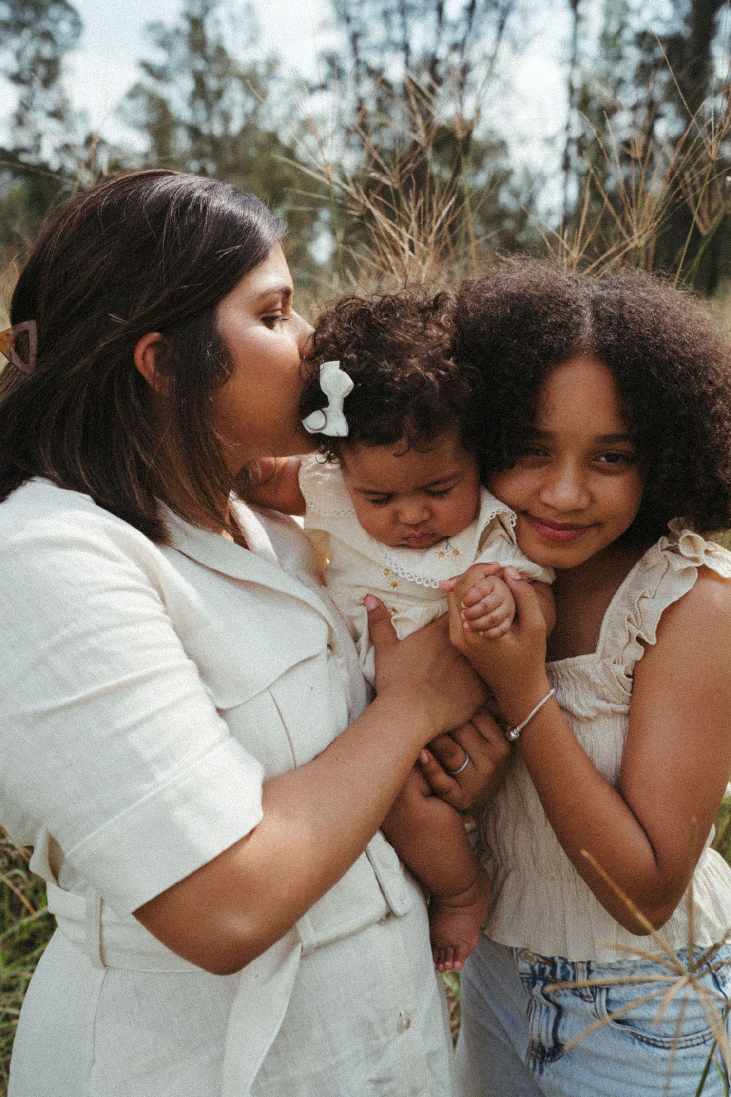 Intimate family photo showing close embraces and laughter in an outdoor setting.