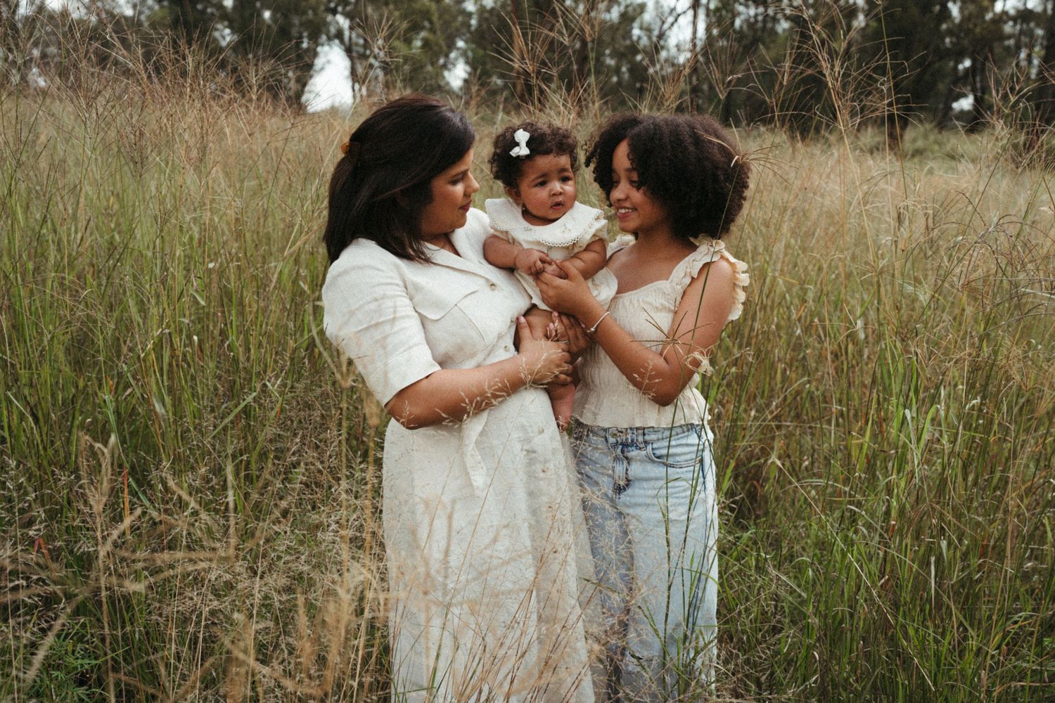 Family wearing white outfits poses together in a grassy field during golden hour.
