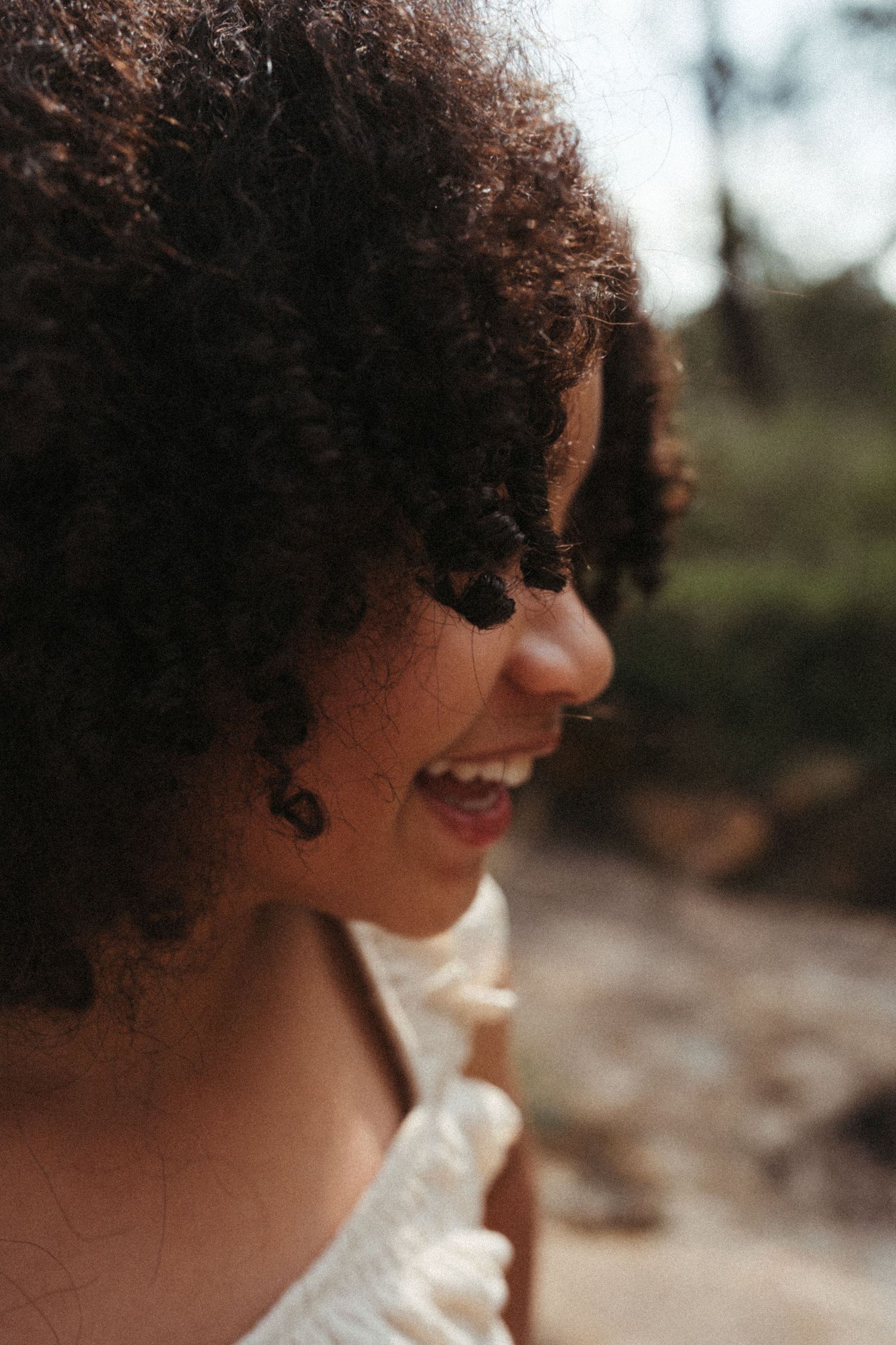 Profile view of curly-haired figure smiling in natural sunlight.