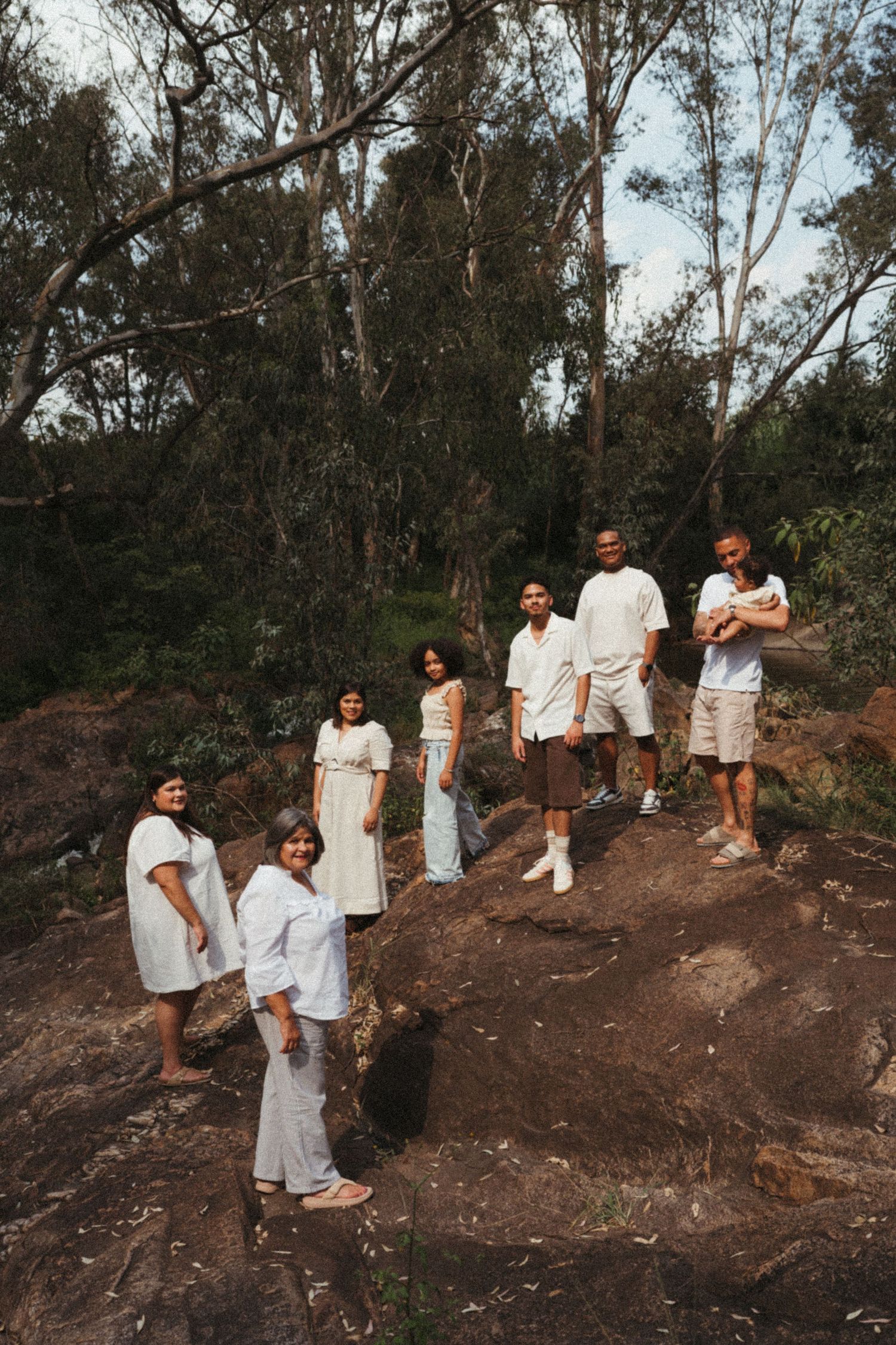 Family photo session on a hillside with everyone dressed in white and beige outfits.