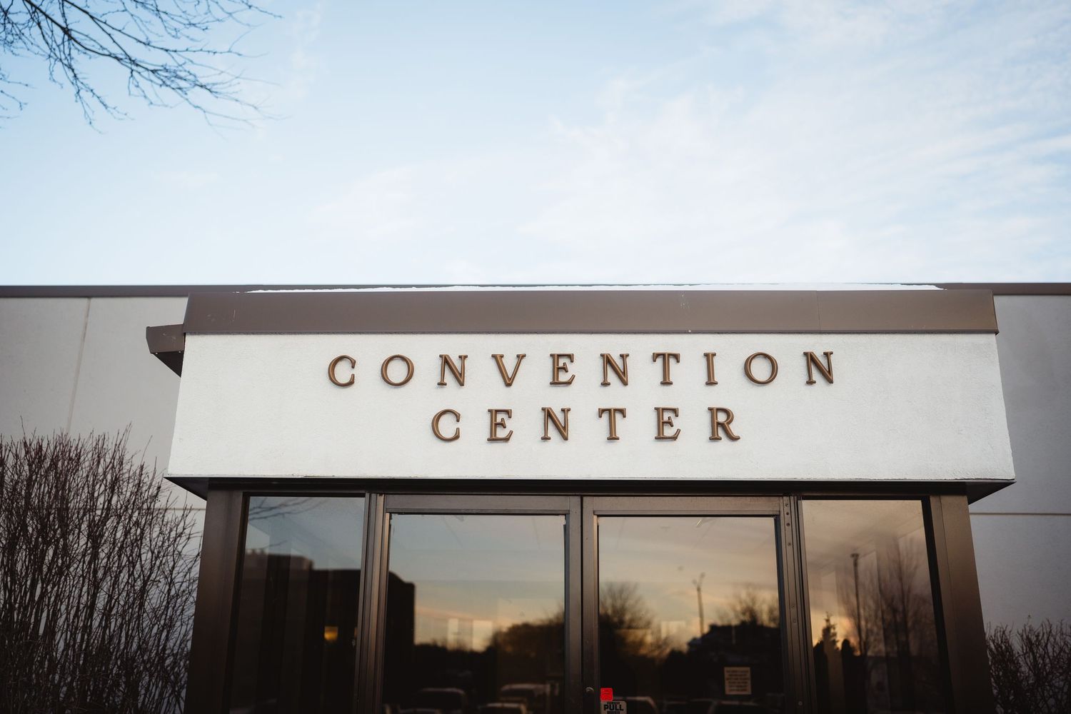 Three signs mounted on a white building exterior spell out 'CONVENTION CENTER' against a cloudy sky.