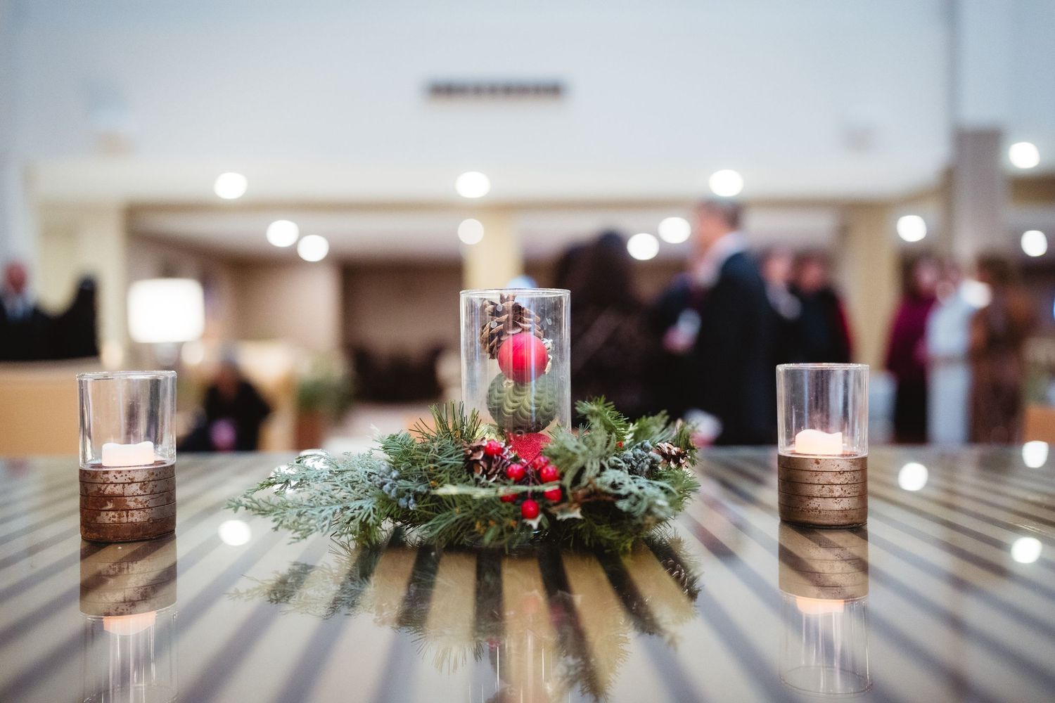 Holiday centerpiece with evergreen branches and red berries surrounded by glowing candles on a wooden table.