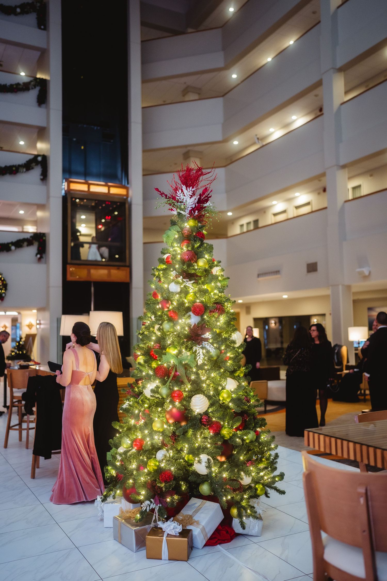 Decorated Christmas trees with twinkling lights and red ornaments in a modern shopping mall atrium.